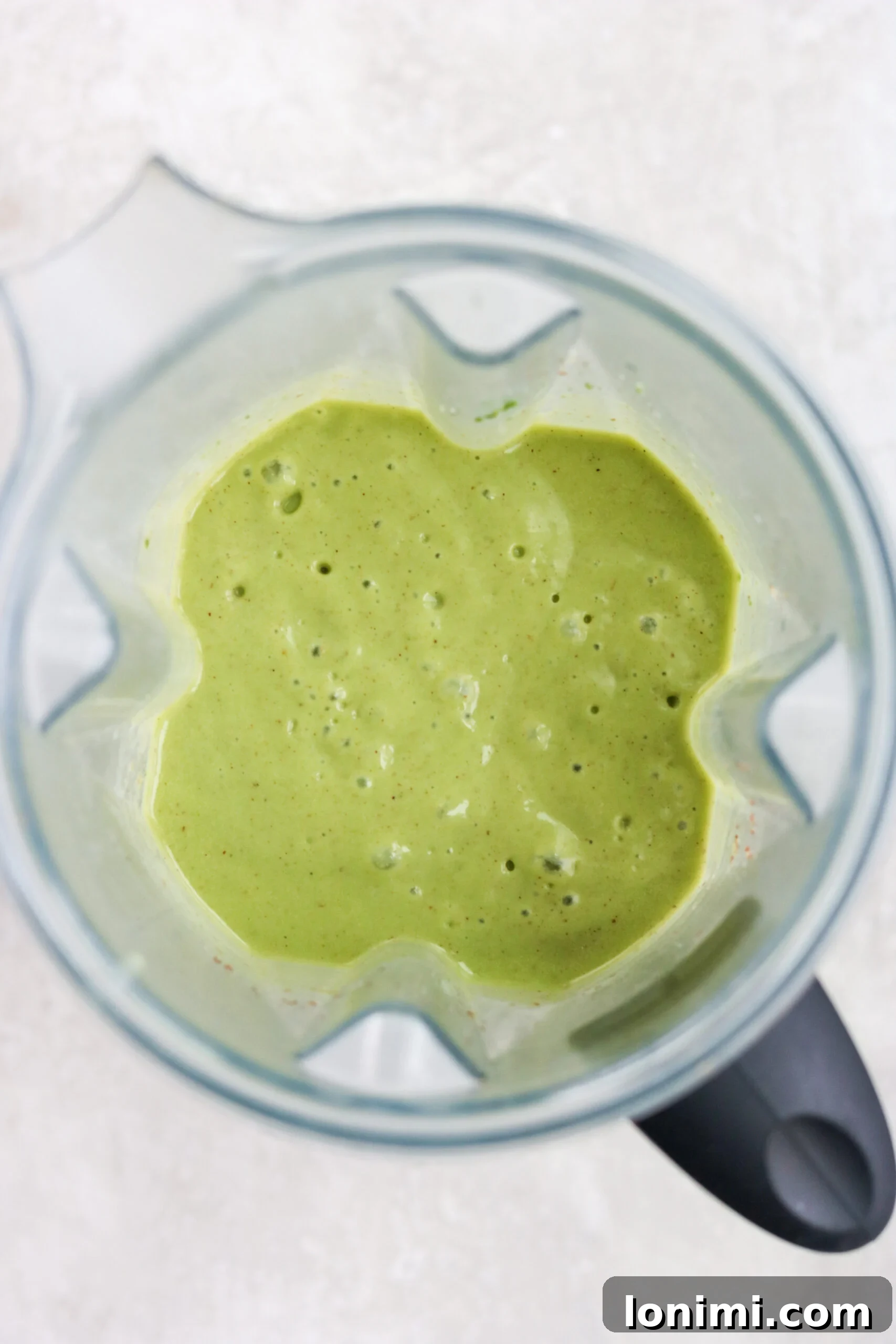 A freshly blended Green Goddess Smoothie in a glass, with a Vitamix blender in the background, showcasing its smooth texture.