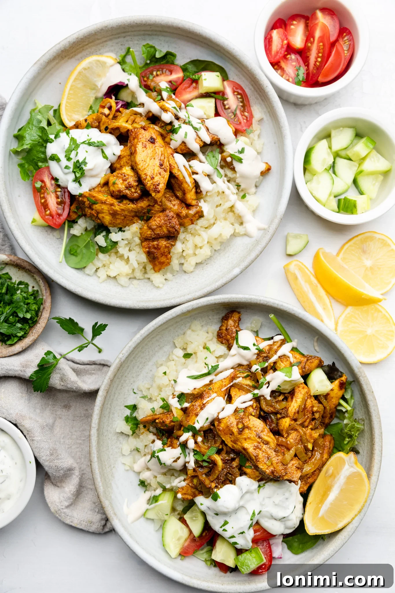 Two vibrant chicken shawarma bowls generously drizzled with creamy lemon garlic tahini sauce, ready to be enjoyed.