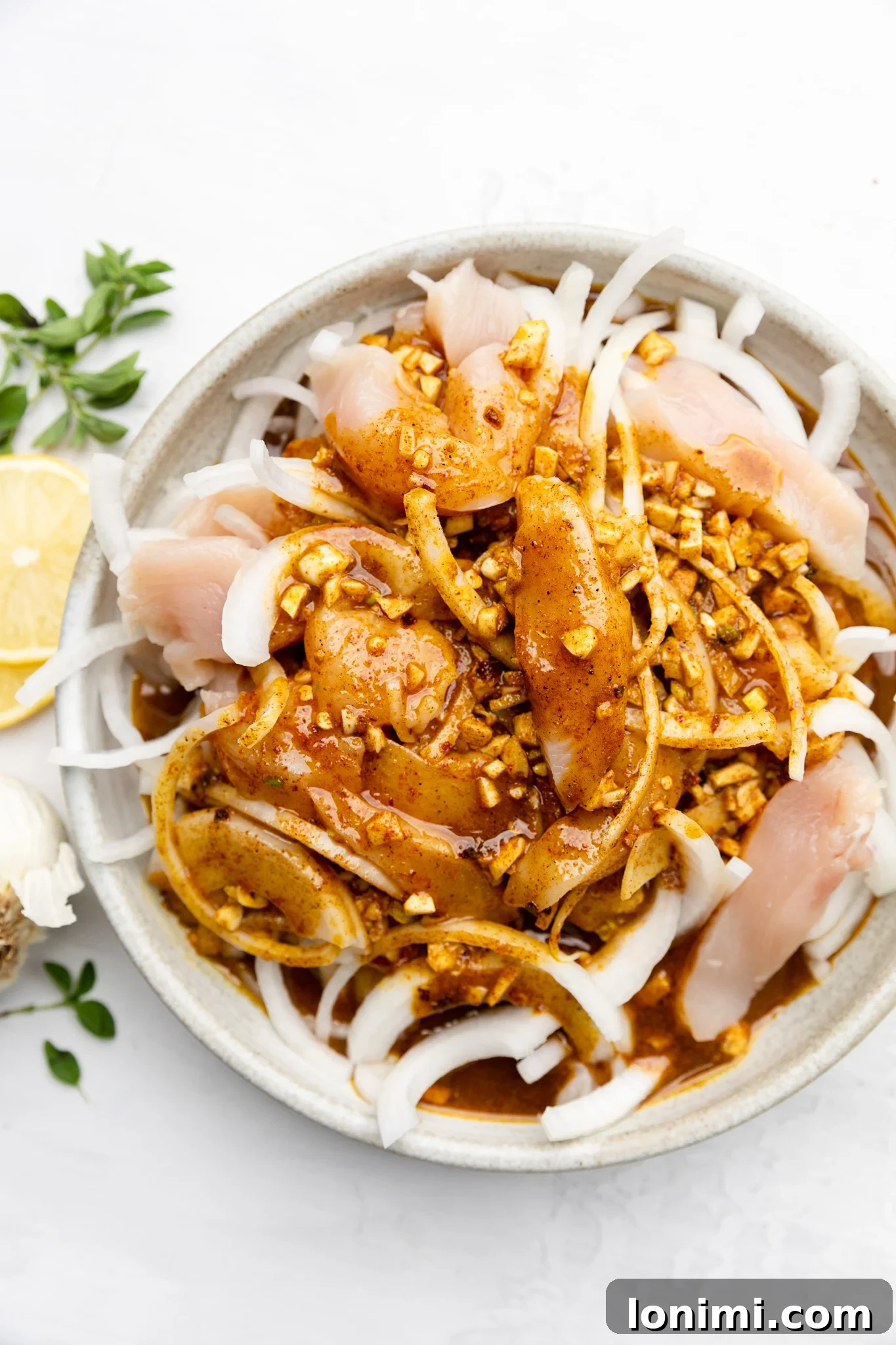 Close-up view of raw chicken strips, sliced onions, and minced garlic marinating together in a large mixing bowl, ready to absorb rich shawarma flavors.