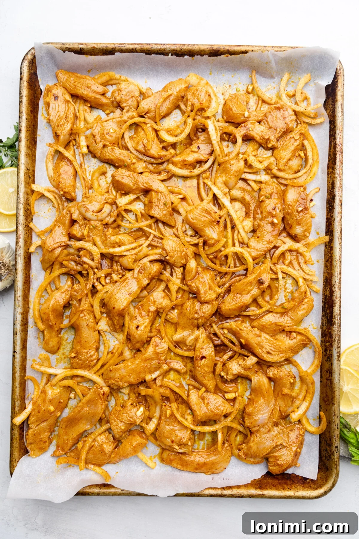Thinly sliced chicken and onions generously coated in shawarma marinade, spread evenly on a lined baking sheet, ready for the oven.