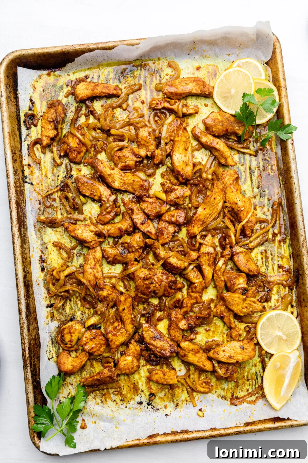 Golden-brown baked chicken shawarma and caramelized onions fresh out of the oven, still on the lined baking sheet, perfectly cooked and fragrant.