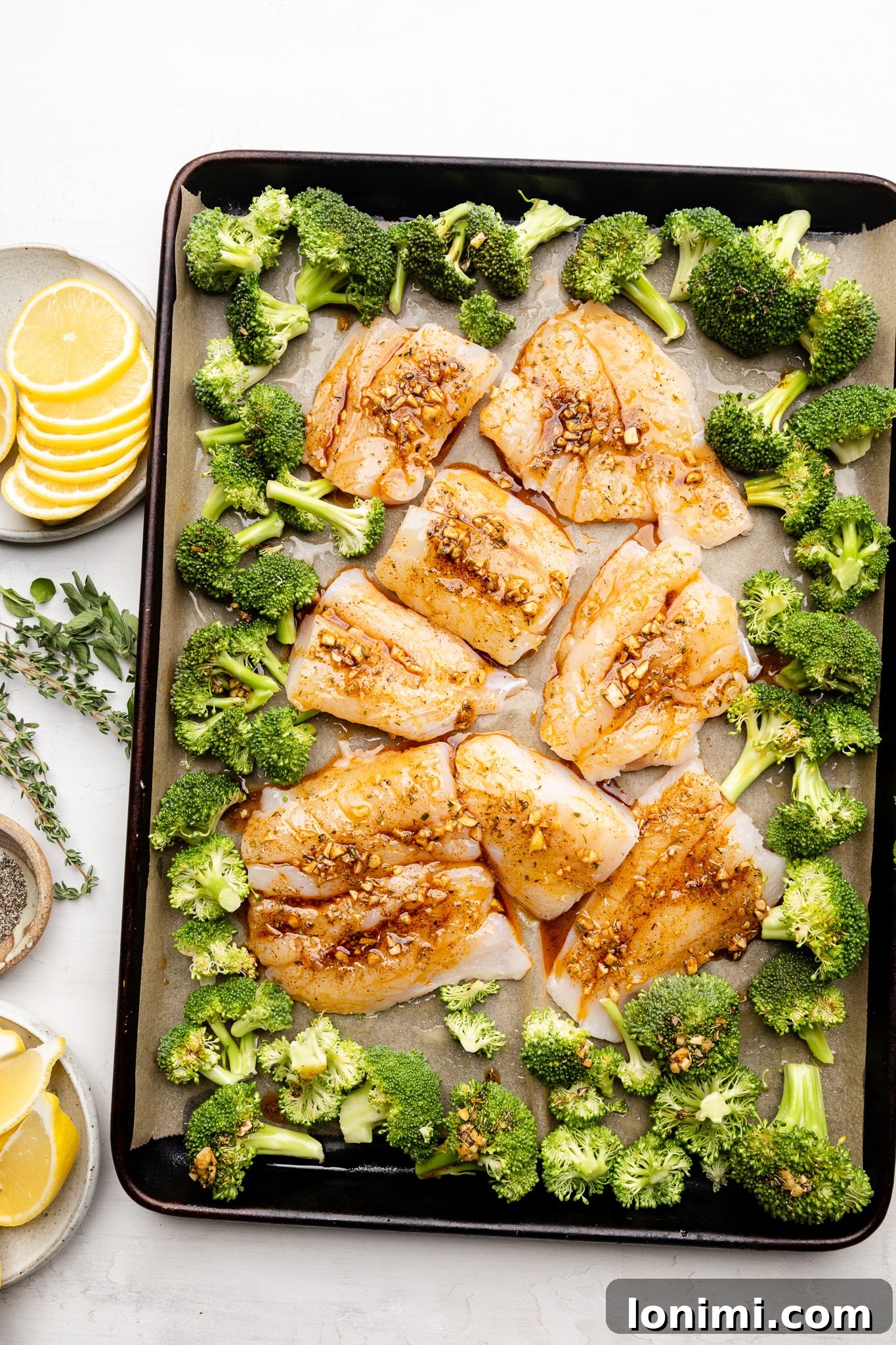 Cod and broccoli spread out on a lined baking sheet, ready for sauce and oven