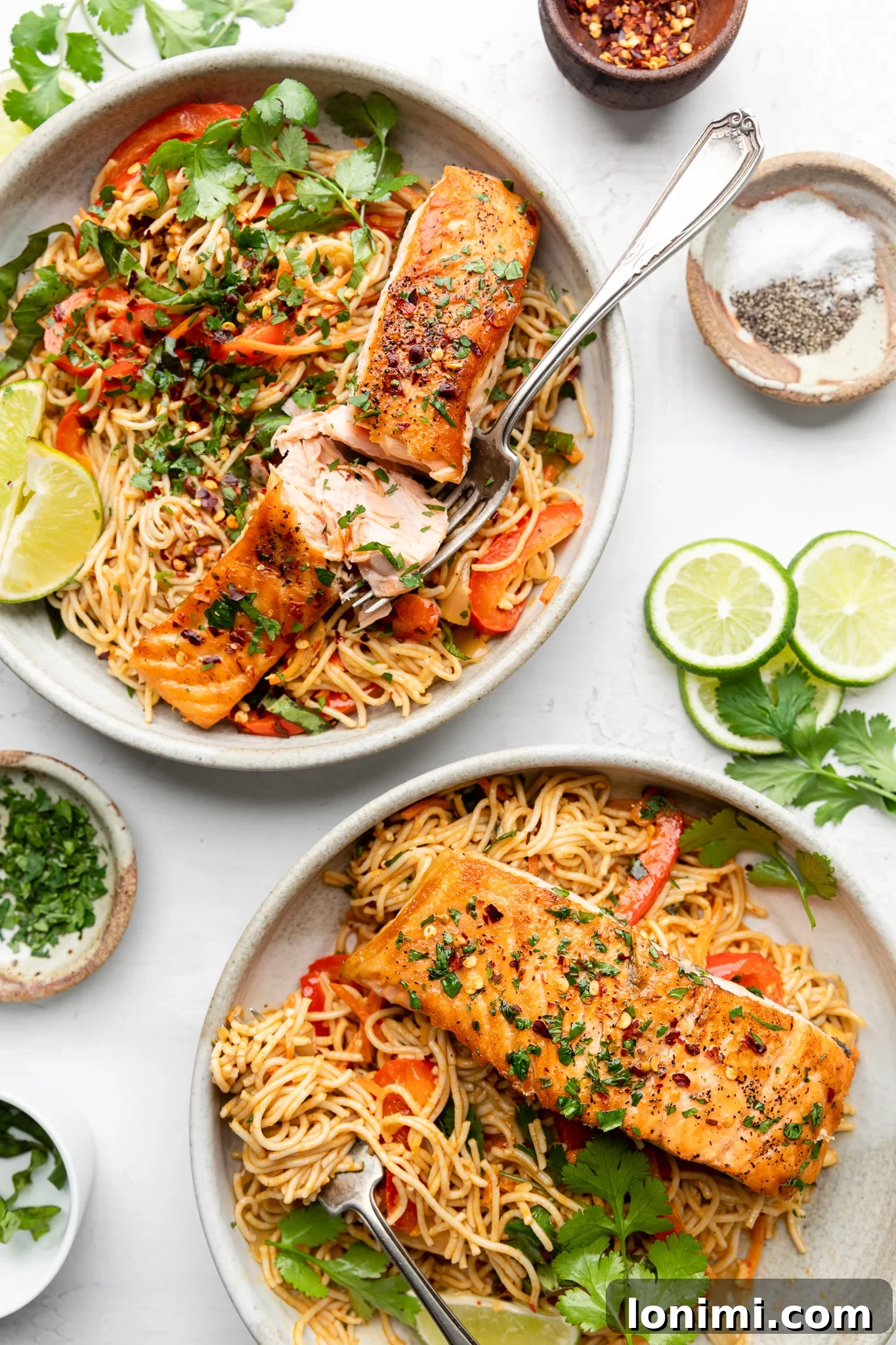 Two plates of Thai Curry Salmon Ramen with lime wedges and cilantro garnish