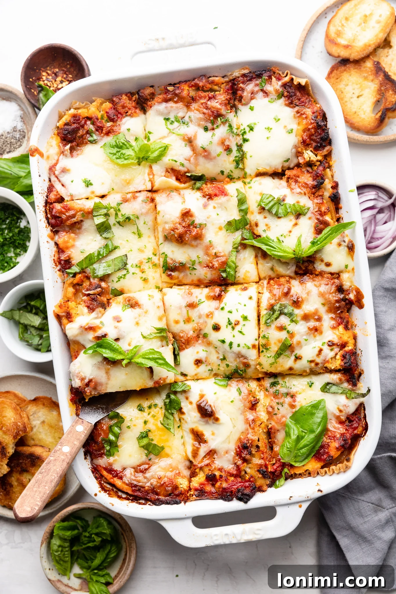 Effortless Allergen-Friendly Lasagna 2 Gluten free lasagna in a white casserole dish with bread and basil on the side, ready to be served