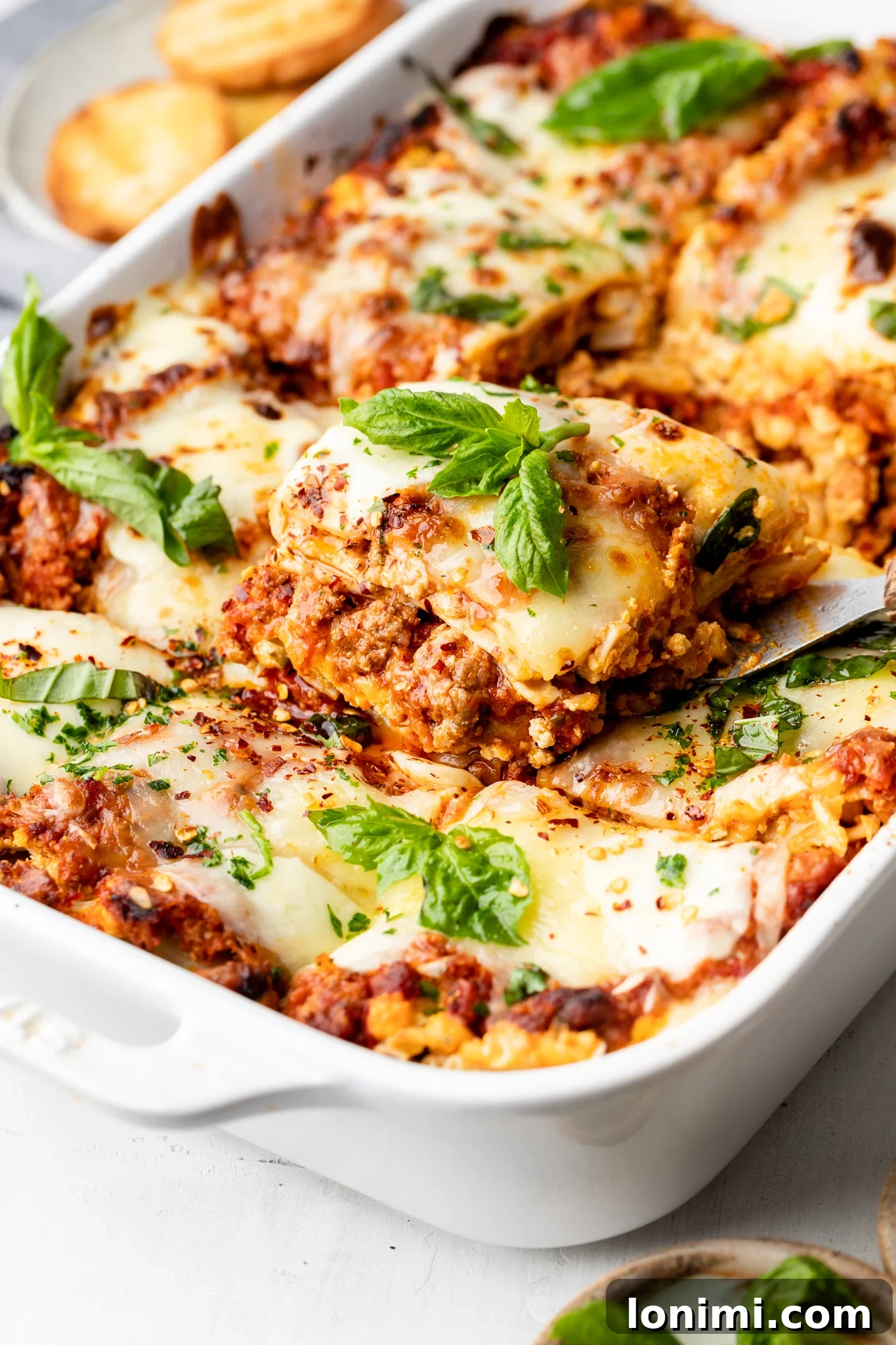 Effortless Allergen-Friendly Lasagna 7 A perfectly portioned slice of gluten-free lasagna garnished with fresh basil, being lifted from the baking dish
