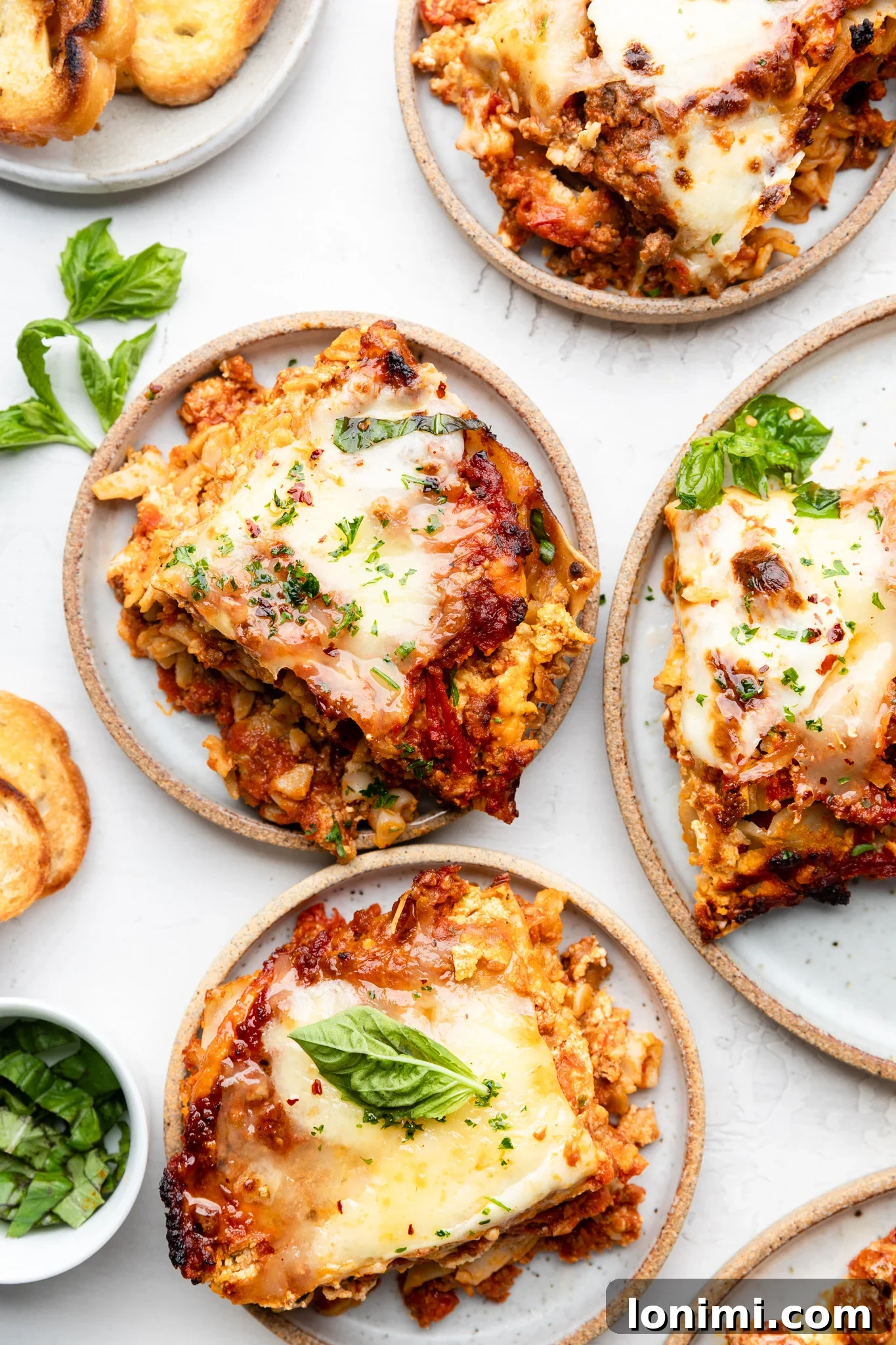 Effortless Allergen-Friendly Lasagna 8 Four individual servings of gluten-free lasagna, each topped with a sprig of fresh basil, presented on white plates