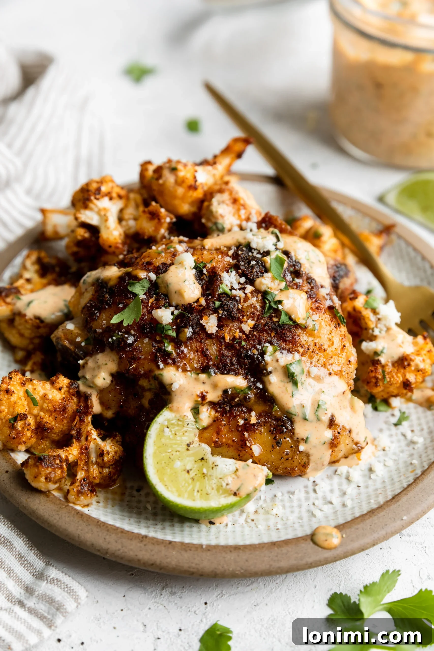 Sheet Pan Fiesta Bowls with Chicken and Roasted Cauliflower 6 a close of up the roasted cauliflower and crispy chicken thighs next to a lime wedge and a bowl of sauce