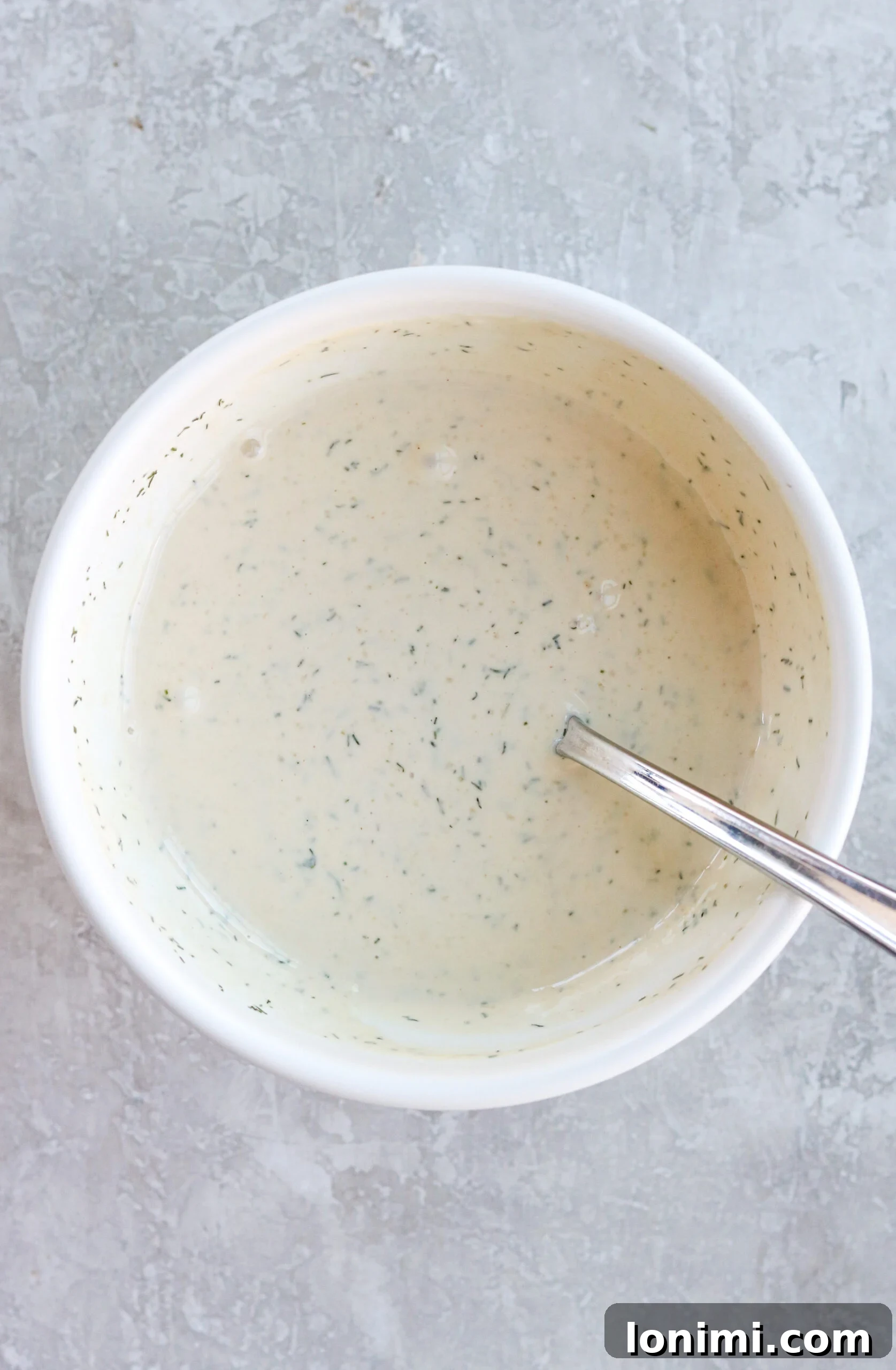 Creamy mayonnaise sauce mixture in a white bowl with a silver spoon.