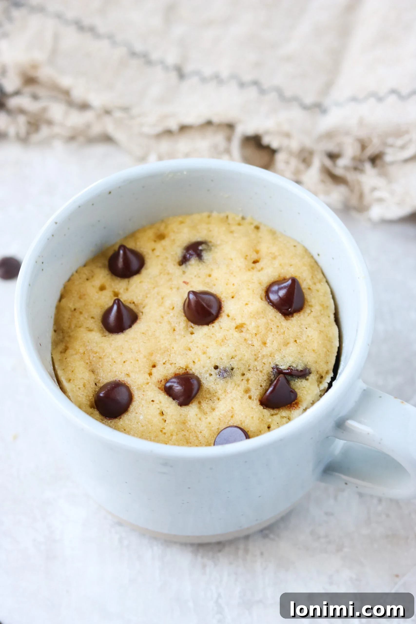 A close-up of a white mug filled with a perfectly cooked chocolate chip mug cake, showing its moist interior.