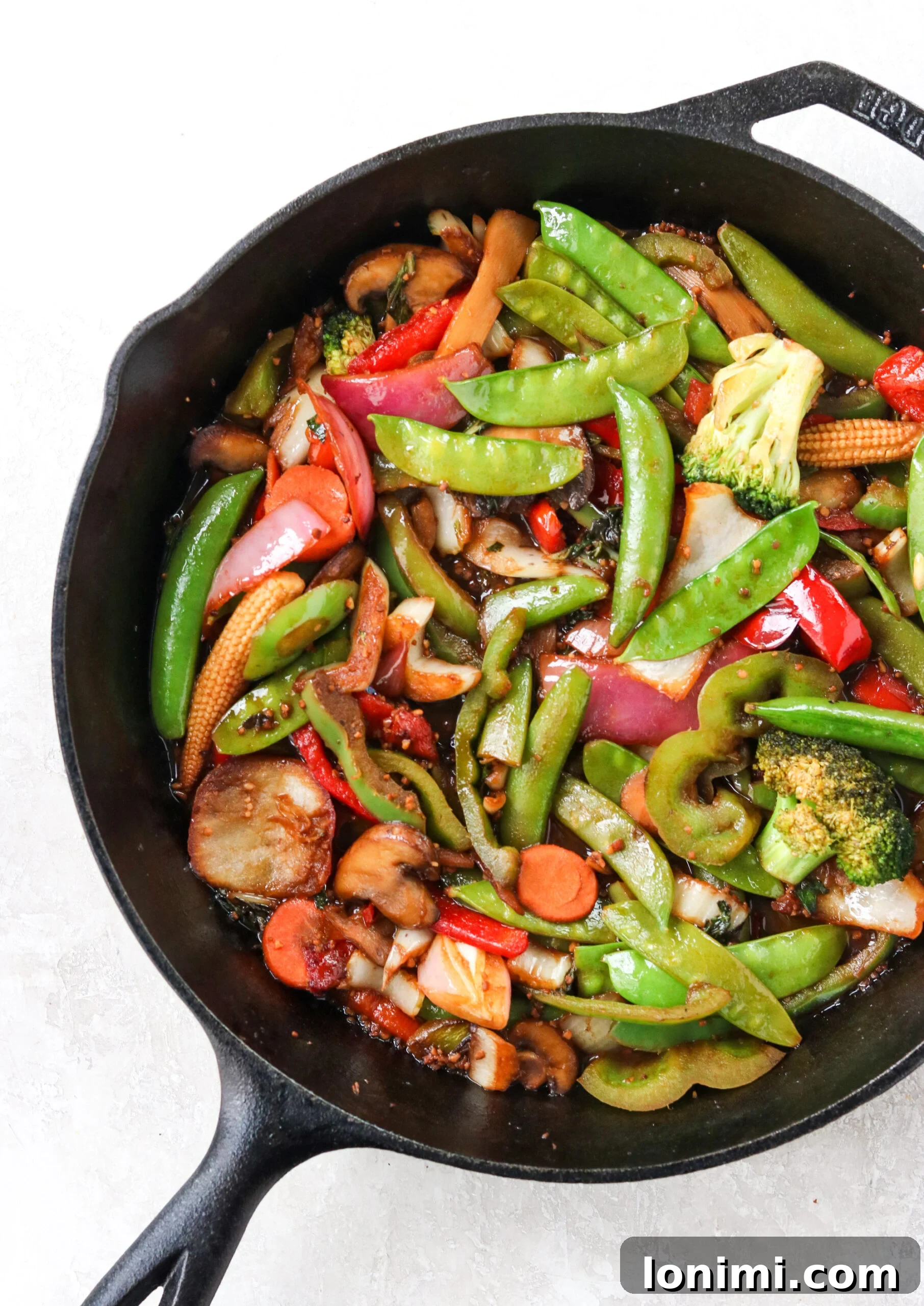 A close-up of vibrant, stir-fried vegetables glistening in a rich brown sauce within a black cast iron skillet.