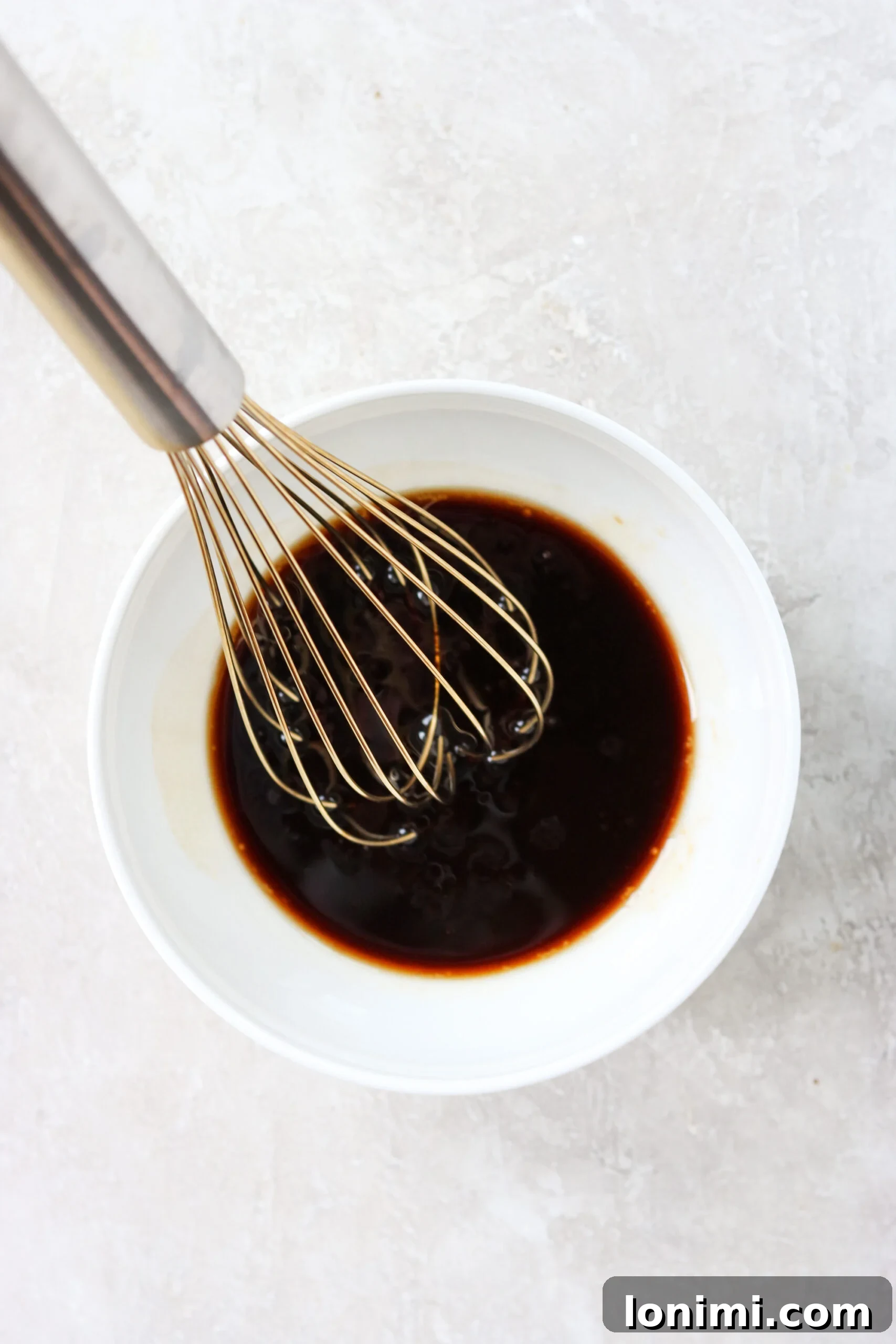 A hand whisking homemade stir fry sauce in a white bowl, showing a smooth, rich consistency.