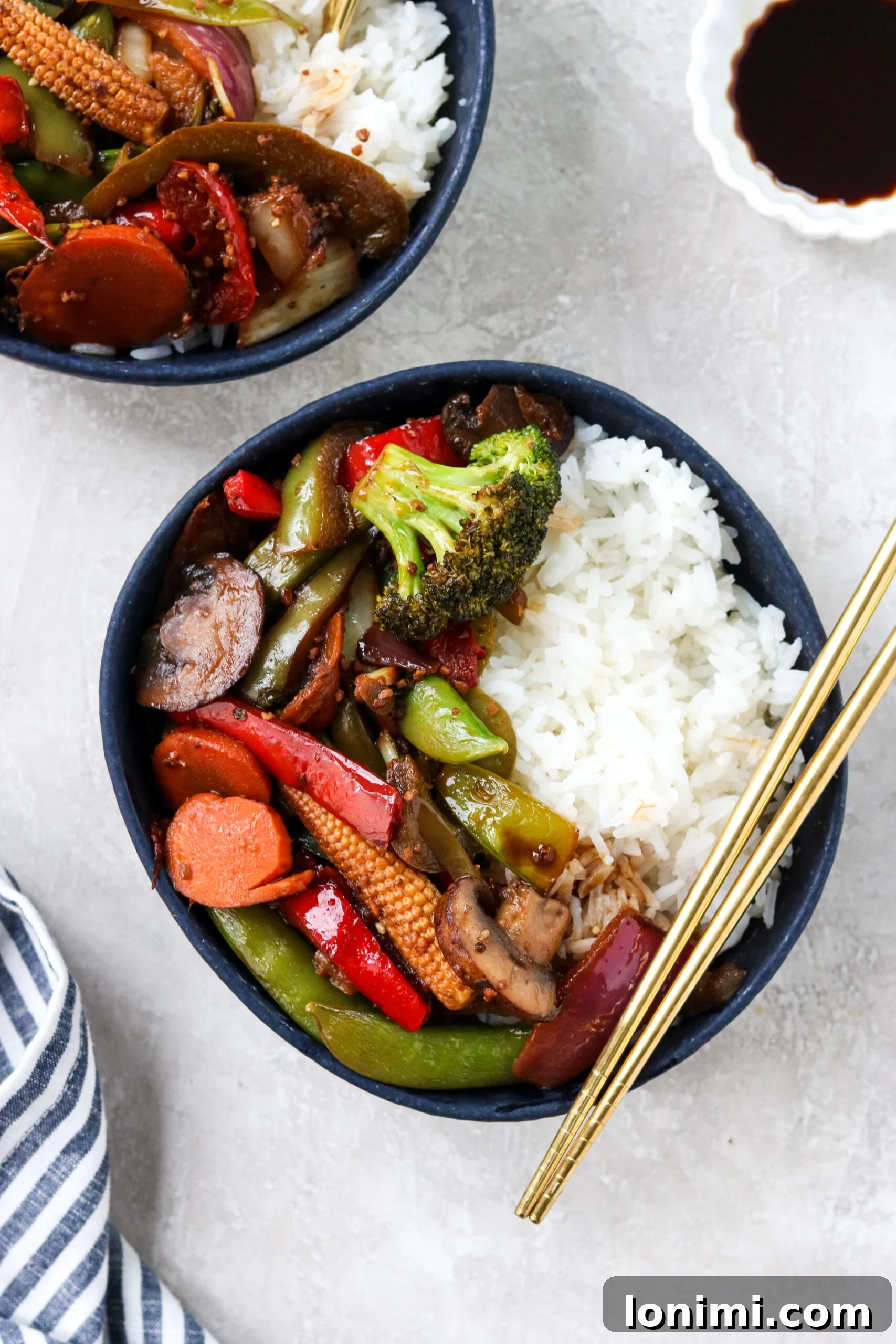 Two blue ceramic bowls filled with white rice, generously topped with vibrant Pad Pak vegetable stir fry, ready to be enjoyed.