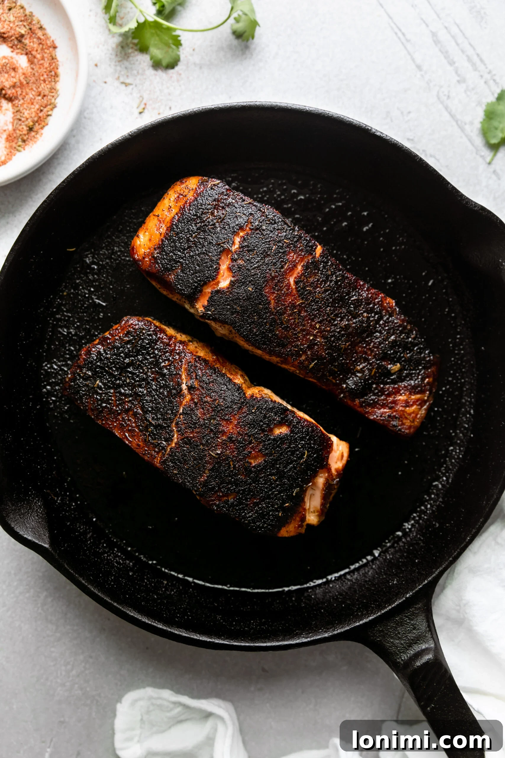 Tropical Blackened Salmon Tacos 4 a cast-iron skillet with two pieces of blackened salmon cooking.
