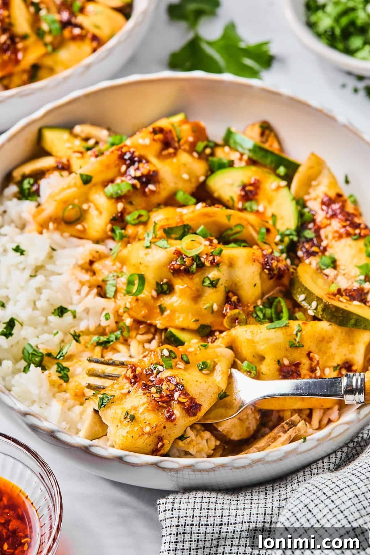 Close-up of gluten-free dumpling bake served over white rice, topped with sliced green onions and sesame seeds, with a fork stuck into a dumpling