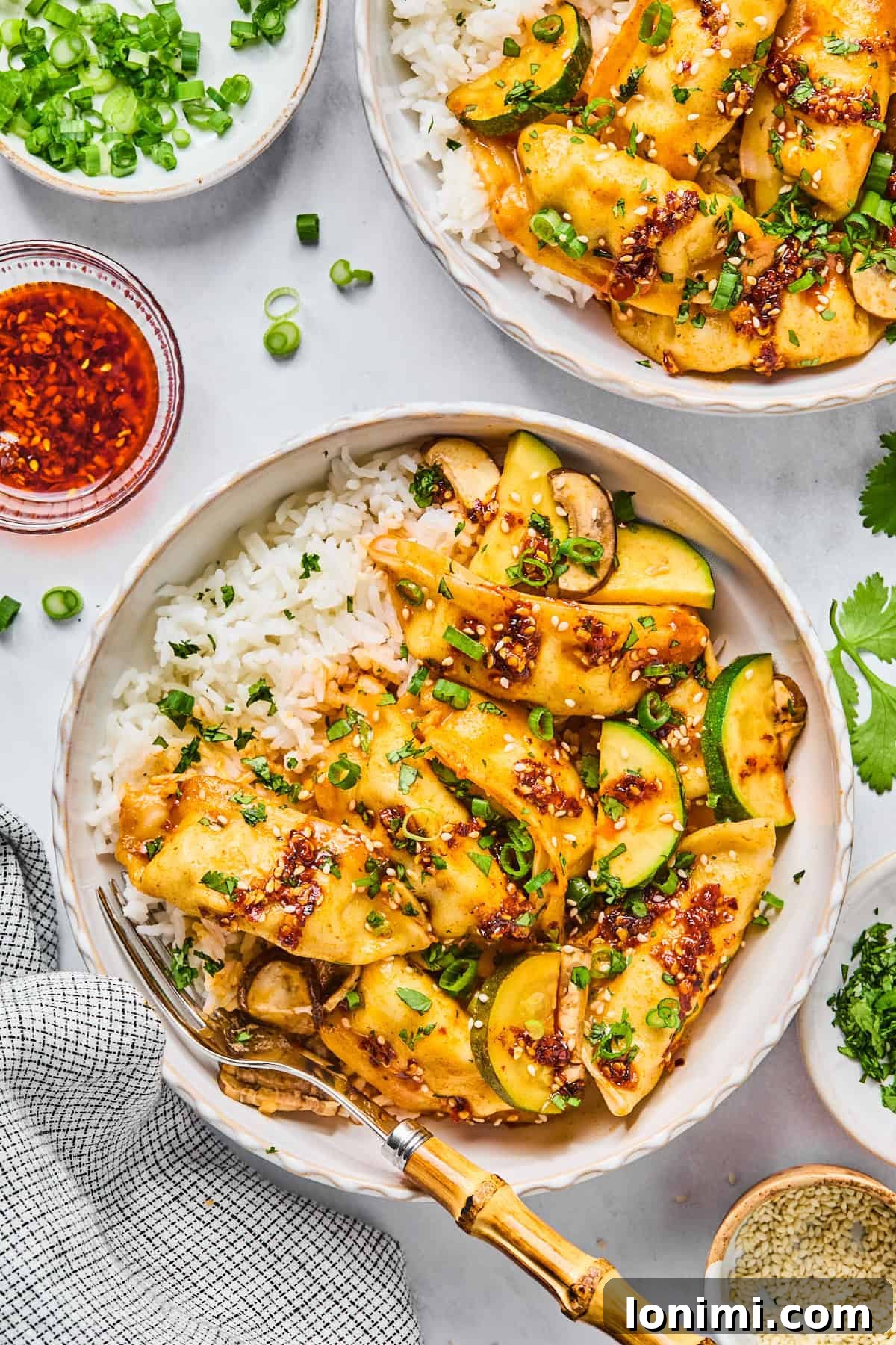 Gluten-free dumpling bake in two bowls served over white rice, topped with sliced green onions and sesame seeds.