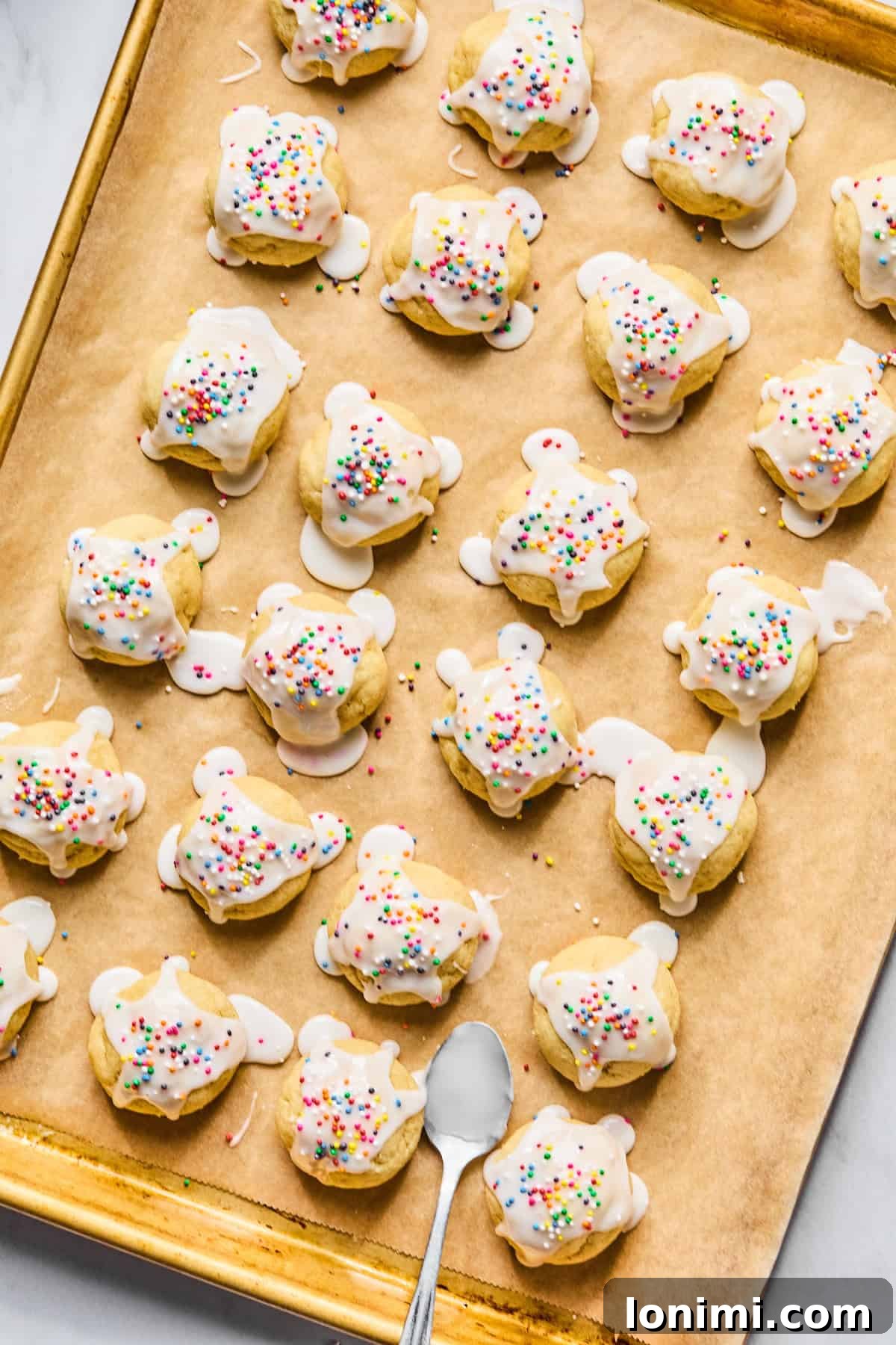 Gluten-free Italian wedding cookies adorned with almond glaze and colorful rainbow sprinkles, glistening on a parchment-lined baking sheet.