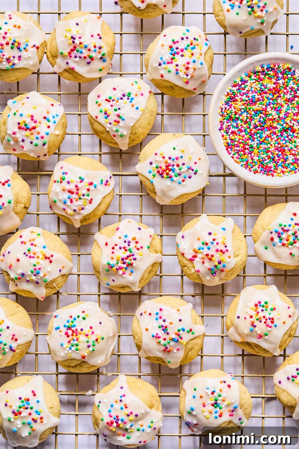 A charming display of gluten free Italian wedding cookies on a wire cooling rack, with a small nesting bowl of rainbow sprinkles nearby.