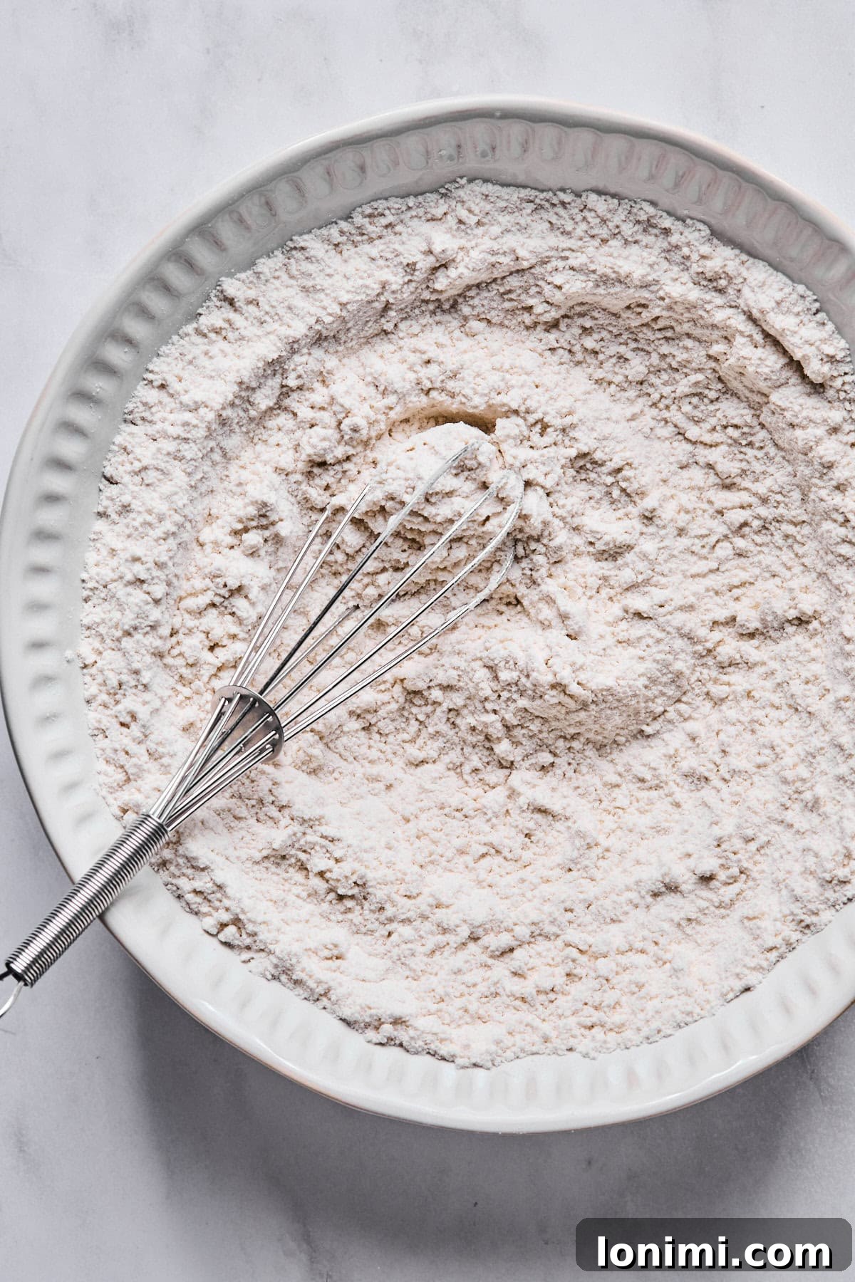 A medium bowl containing dry ingredients: gluten-free flour, baking powder, and salt, perfectly mixed.