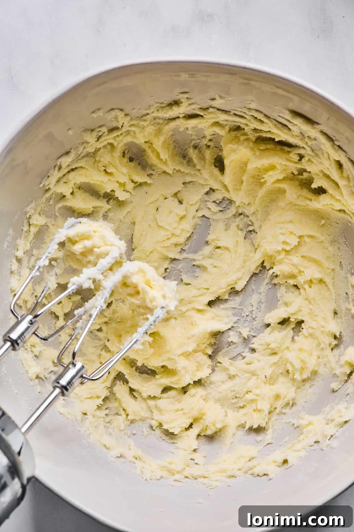 A large mixing bowl showcasing softened butter and granulated sugar creamed together to a light and fluffy consistency using an electric mixer.