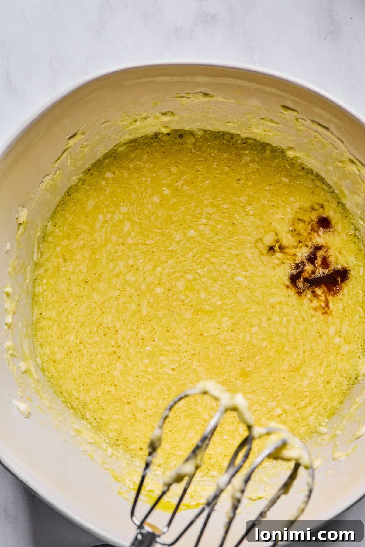 Eggs, vanilla extract, and almond extract fully incorporated into the batter in a large mixing bowl, creating a smooth and aromatic mixture.