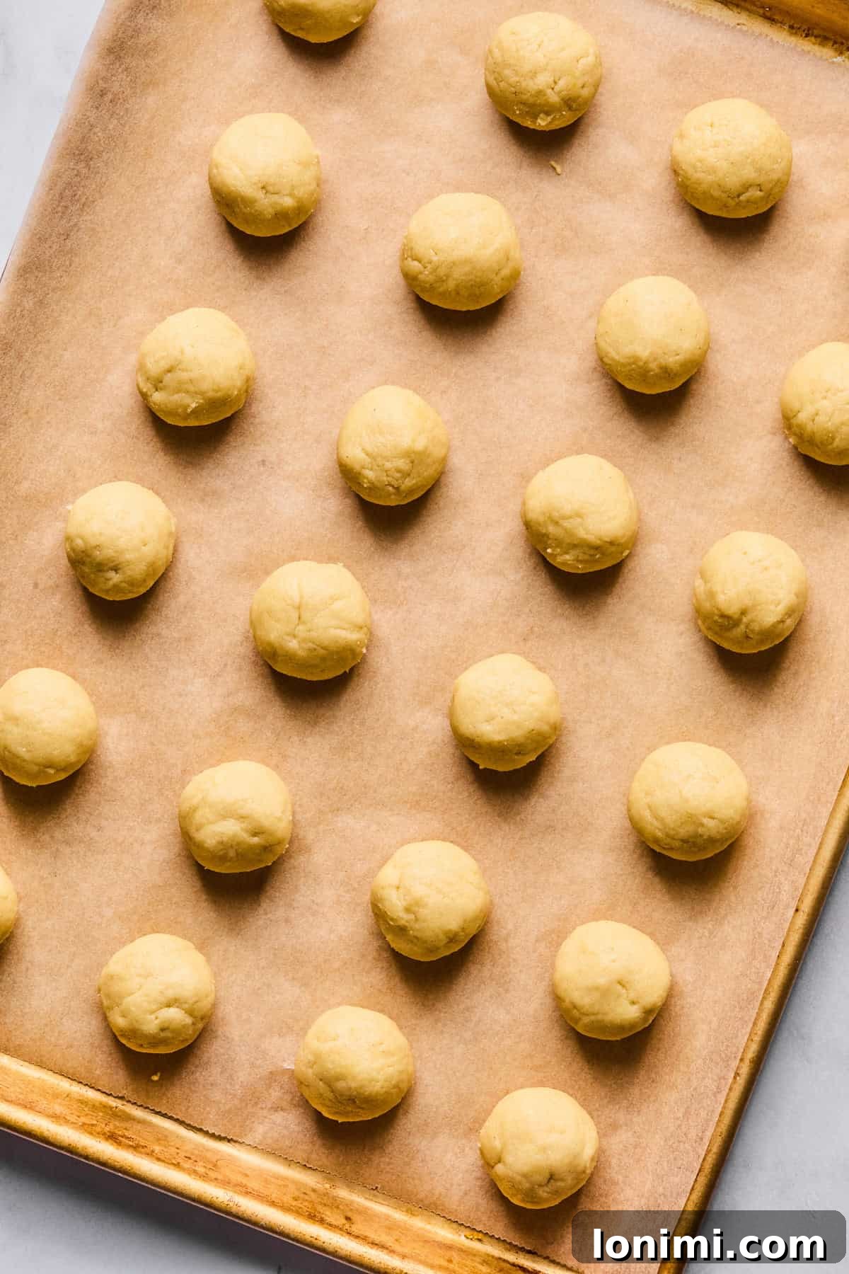 Italian wedding cookie dough neatly rolled into 24 uniform balls and arranged on a parchment-lined baking sheet, prepared for chilling.
