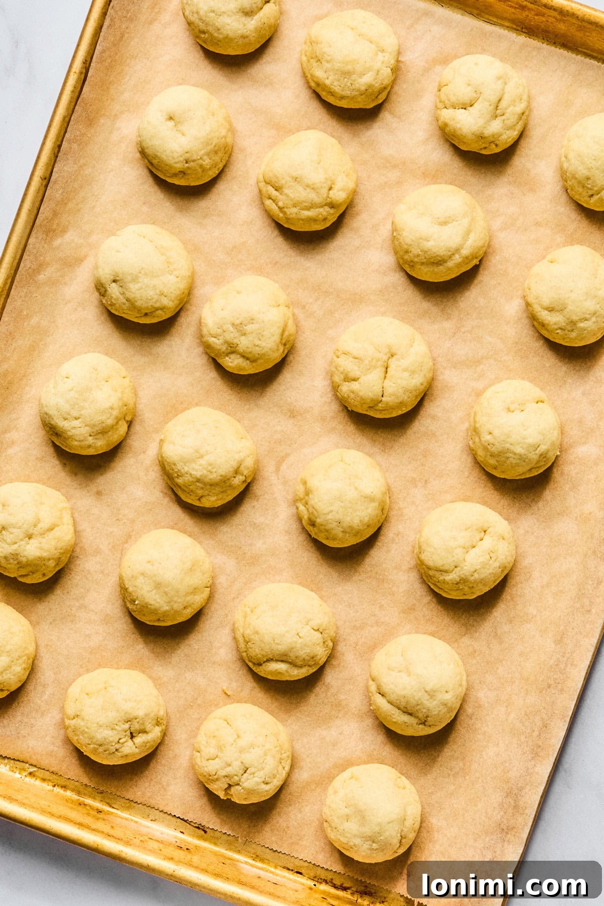Freshly baked gluten free Italian wedding cookies cooling on the parchment-lined baking sheet, perfectly set and ready for glazing.
