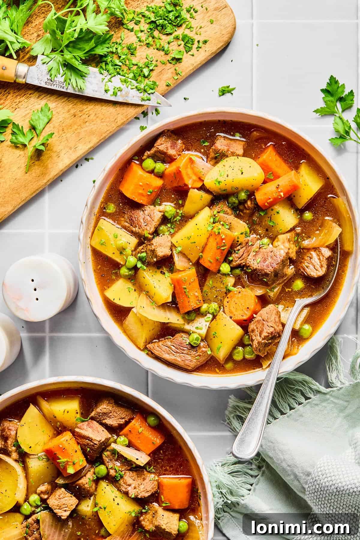 Two bowls of slow cooker beef stew on a light gray colored countertop, inviting and ready to be served.