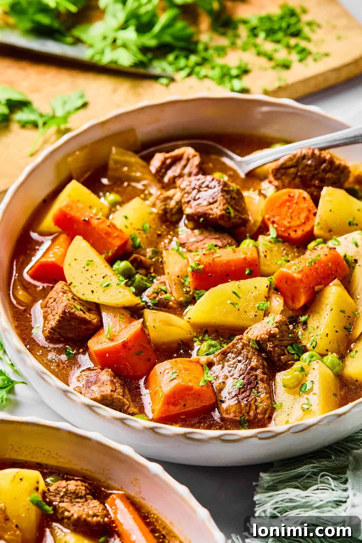 Close-up of a bowl of slow cooker beef stew with a spoon in it, highlighting the rich texture and delicious ingredients.