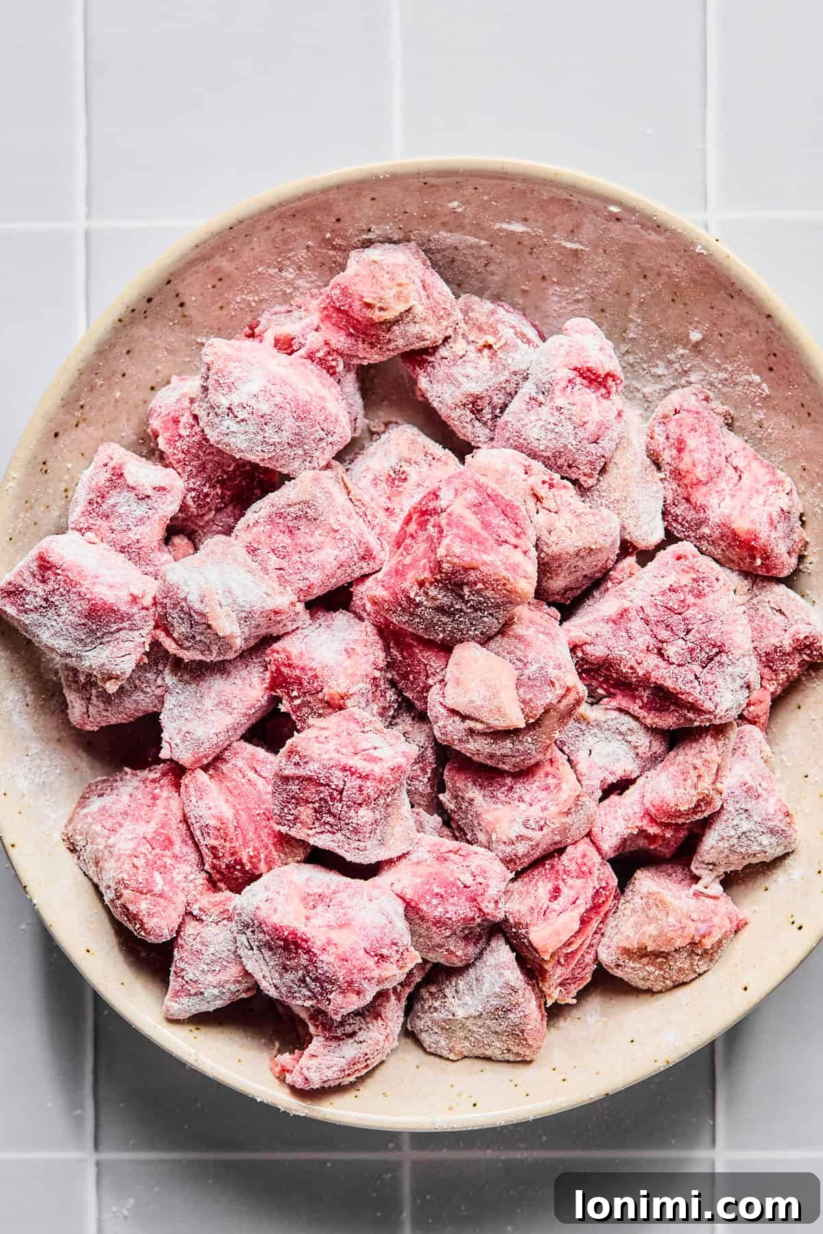 Stew meat in a bowl coated with gluten-free flour and salt and pepper, ready for searing.