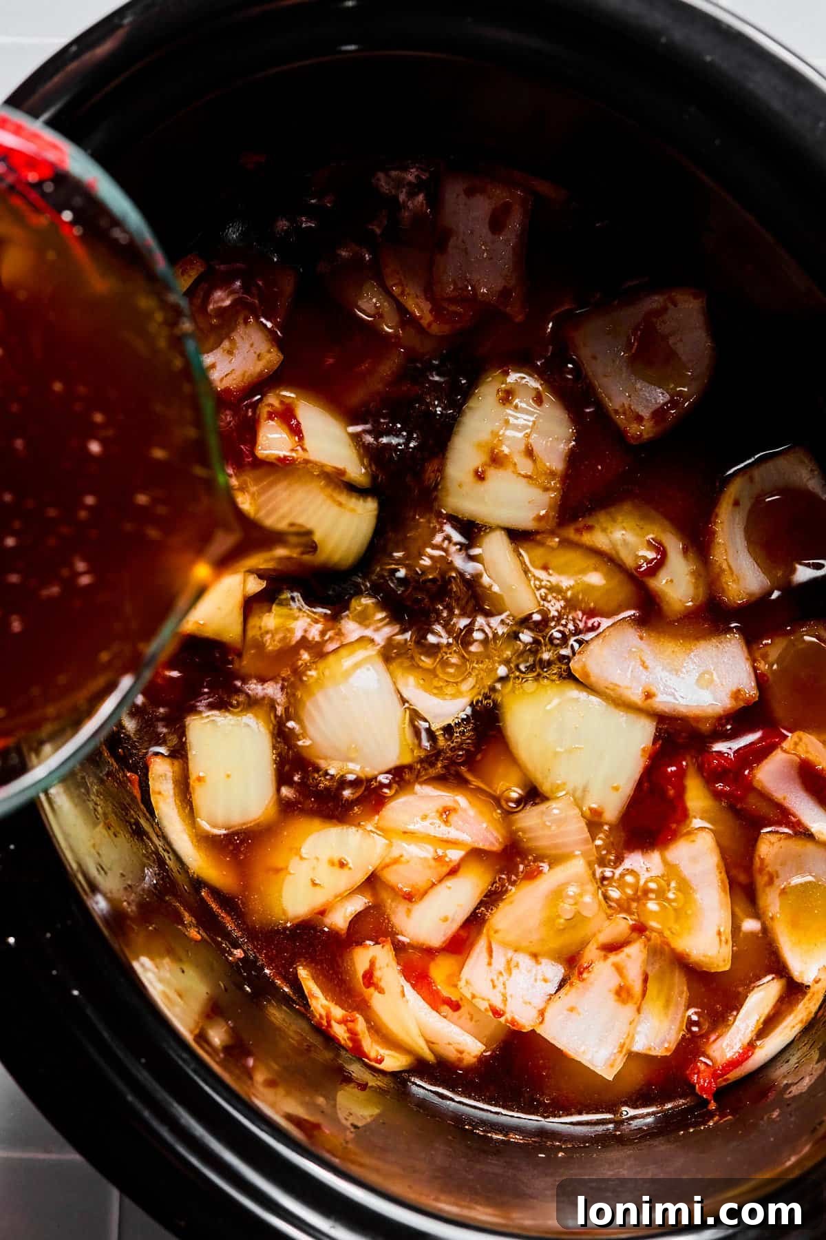 Beef broth being poured into a slow cooker with tomato paste, onions, and garlic, forming the stew base.