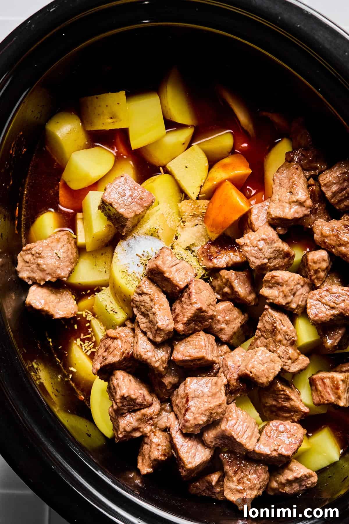 Stew meat, carrots, potatoes, Worcestershire sauce, hot sauce, rosemary, thyme, salt, and pepper carefully arranged in a slow cooker.