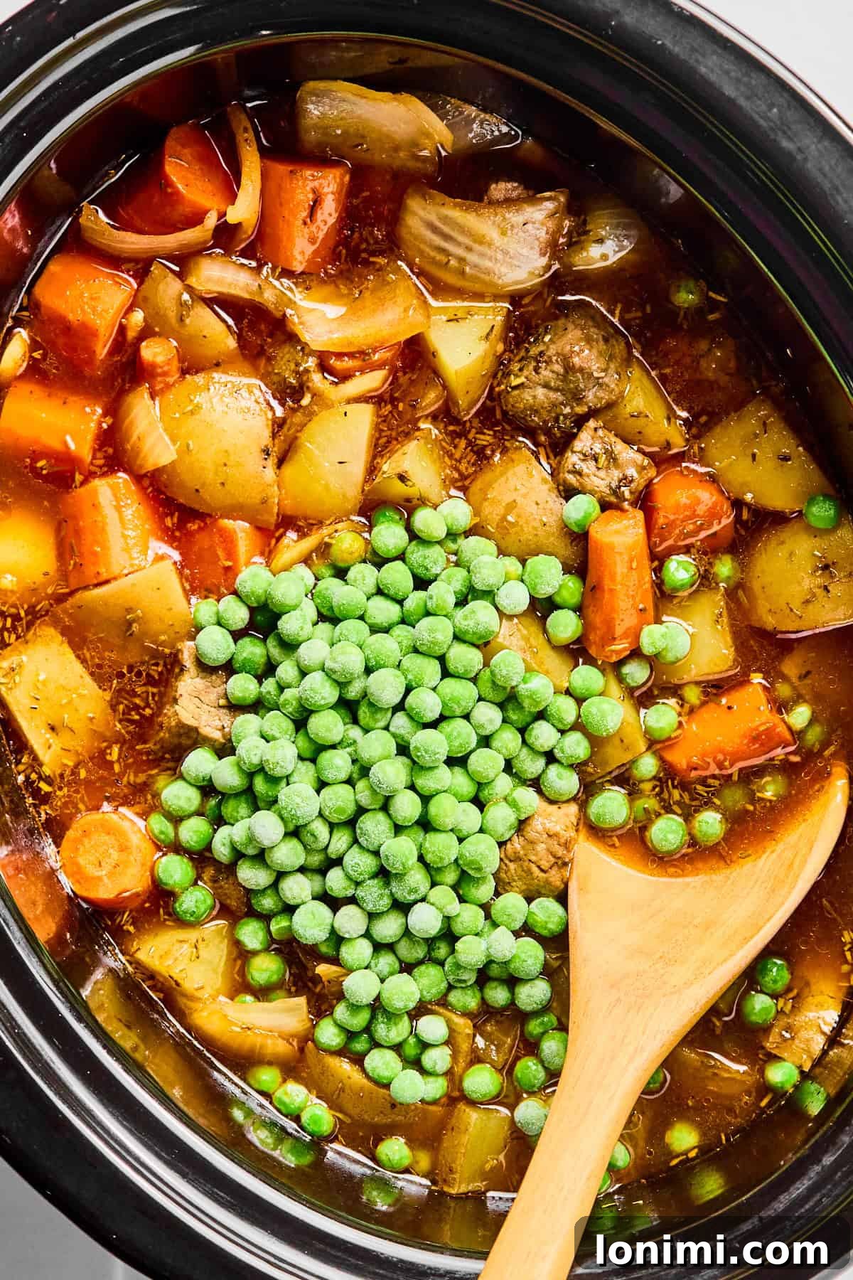 Peas, stew meat, carrots, potatoes, and seasonings simmering in a slow cooker, nearing completion.