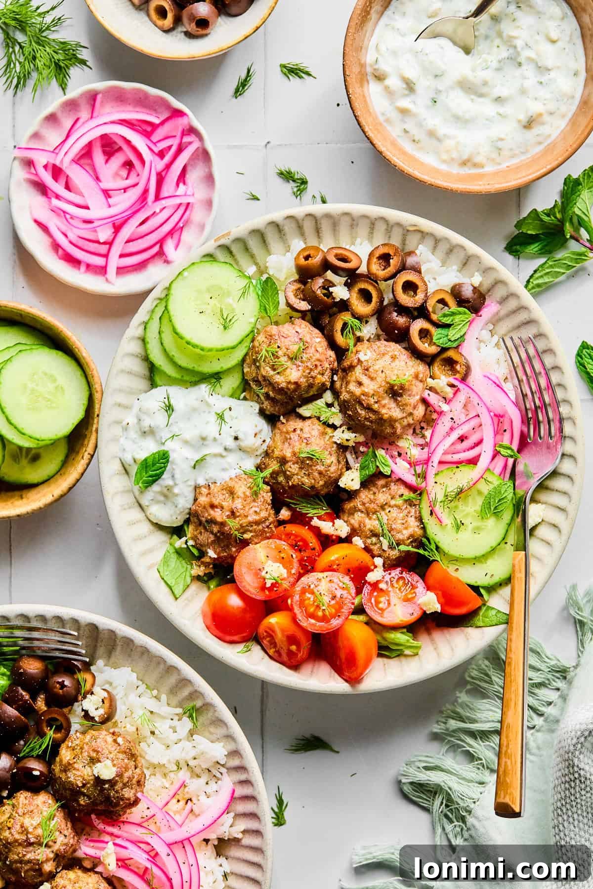 Easy Greek Lamb Meatballs with Zesty Lemon Dill Yogurt 10 Greek lamb meatballs served over rice, surrounded by sliced cucumber, black olives, red onion, cherry tomatoes, fresh herbs, and crumbled feta cheese, with lemon dill yogurt sauce.