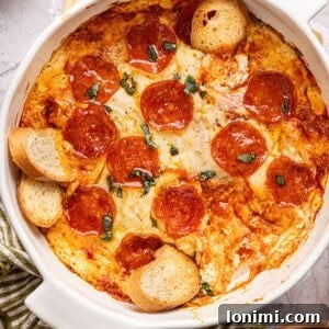 High Protein Pizza Dip in a casserole dish topped with pepperonis and basil, with baguette slices stuck into it, ready to be served.