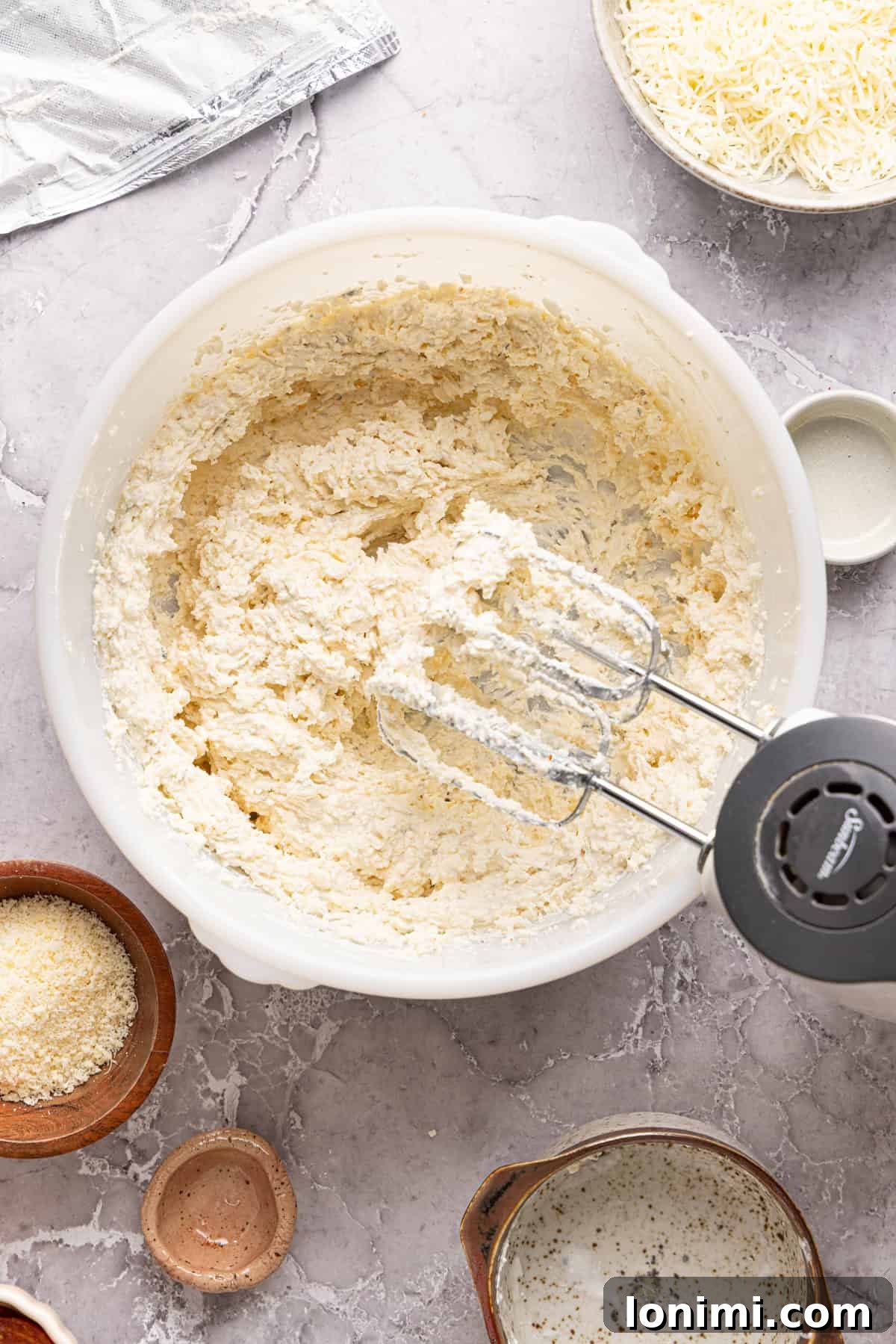 Close-up of a handheld electric mixer actively blending the creamy cheese mixture in a white bowl, ensuring a smooth and lump-free base for the pizza dip.