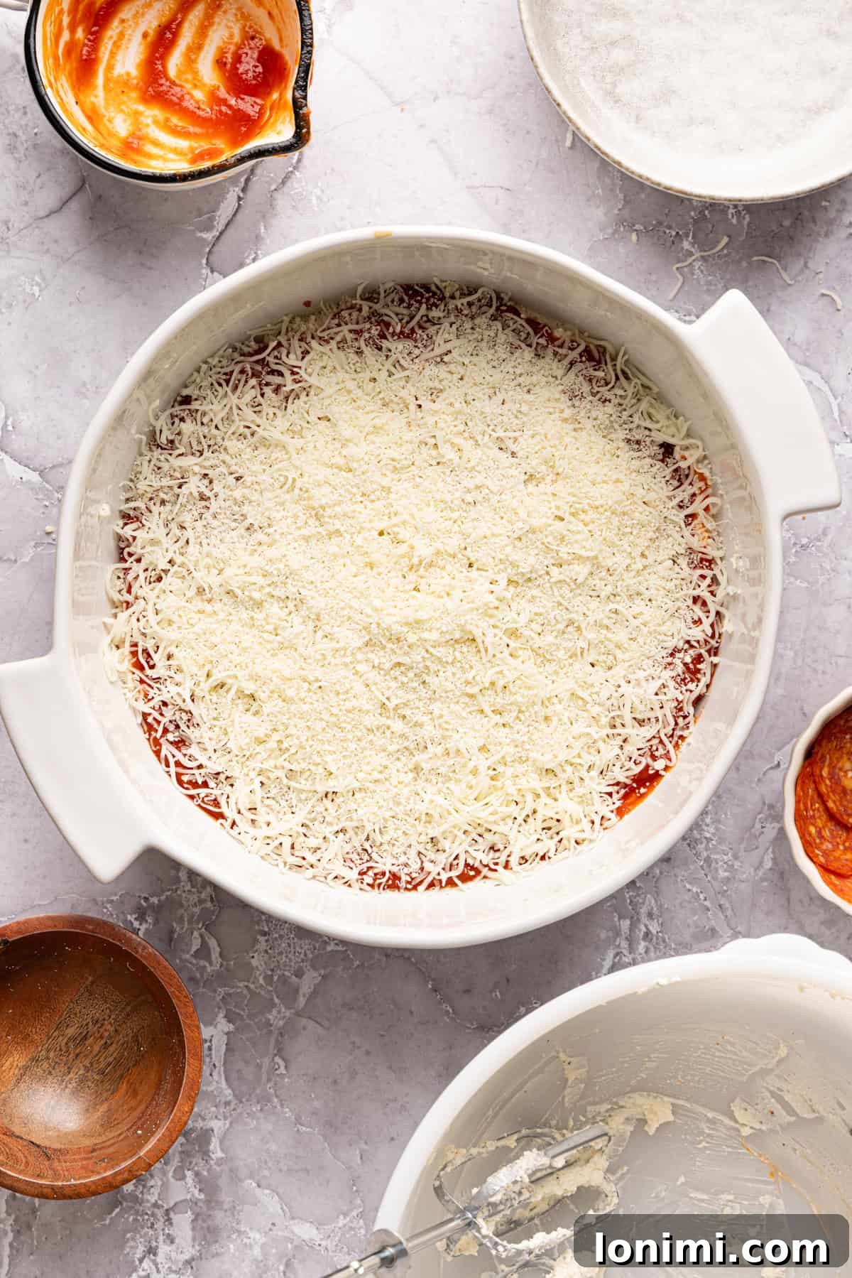 Shredded mozzarella and grated parmesan cheese lightly sprinkled over the pizza sauce layer of the unbaked high protein pizza dip, ready for the final toppings.