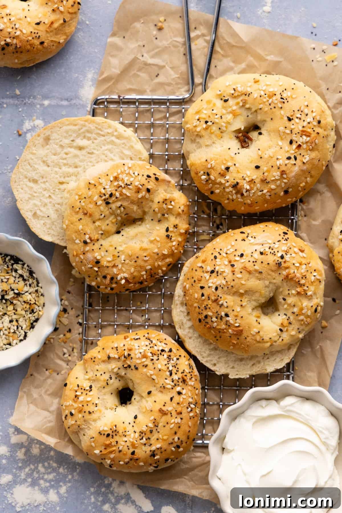 Four cottage cheese bagels on a wire cooling rack with a small bowl of cream cheese next to it. 