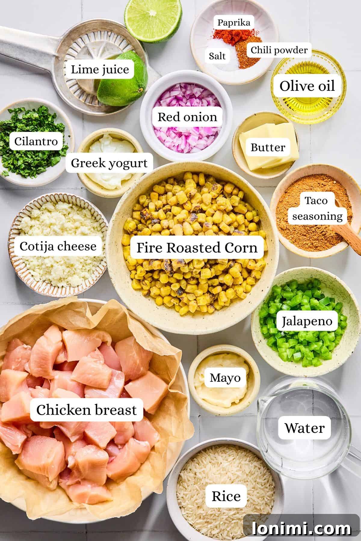 Ingredients for street corn chicken rice bowls labeled and arranged in small bowls on a white countertop.