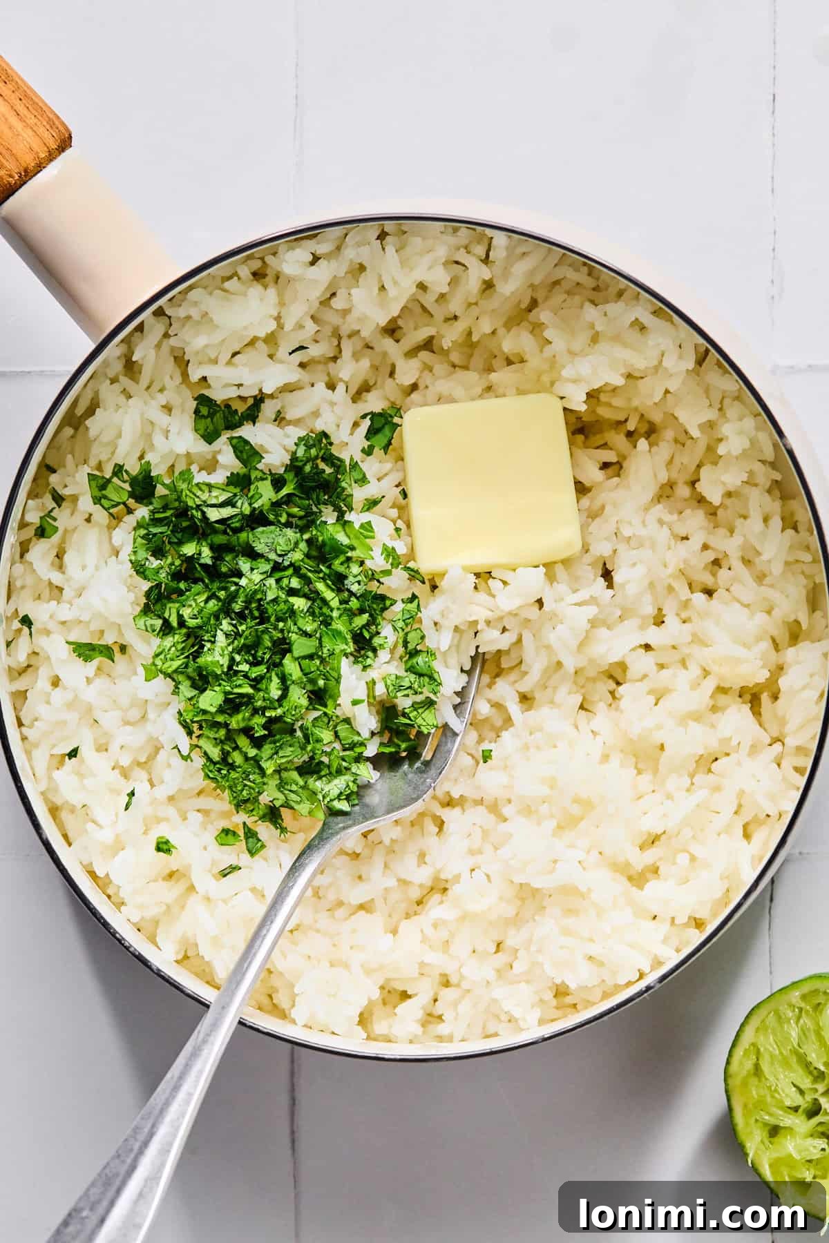 Fluffy cilantro lime rice being mixed with butter, salt, and fresh lime juice in a saucepan.