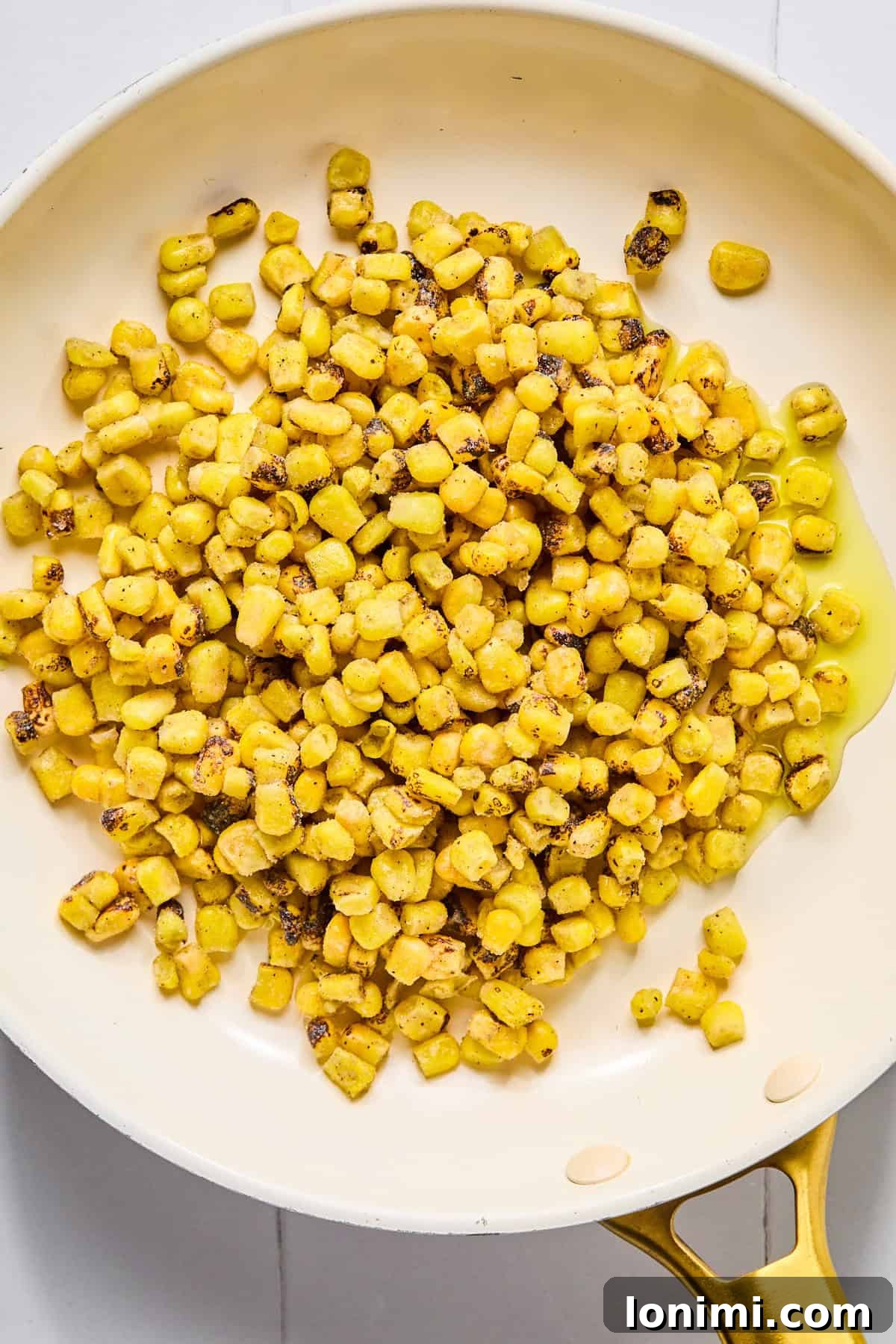 Charred corn cooking in a skillet in oil.