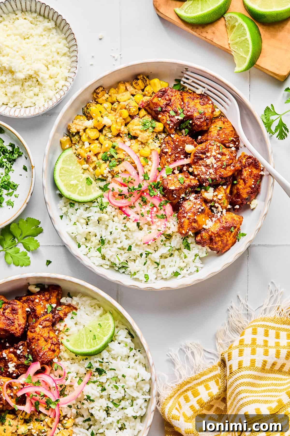 Two street corn chicken rice bowls garnished with cilantro and a lime wedge, with a fork resting inside the main bowl.