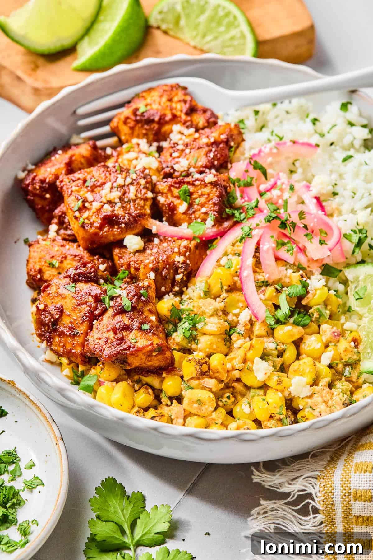 Close-up of a street corn chicken rice bowl with a fork lifting a piece of taco-seasoned chicken, garnished with fresh cilantro and lime.