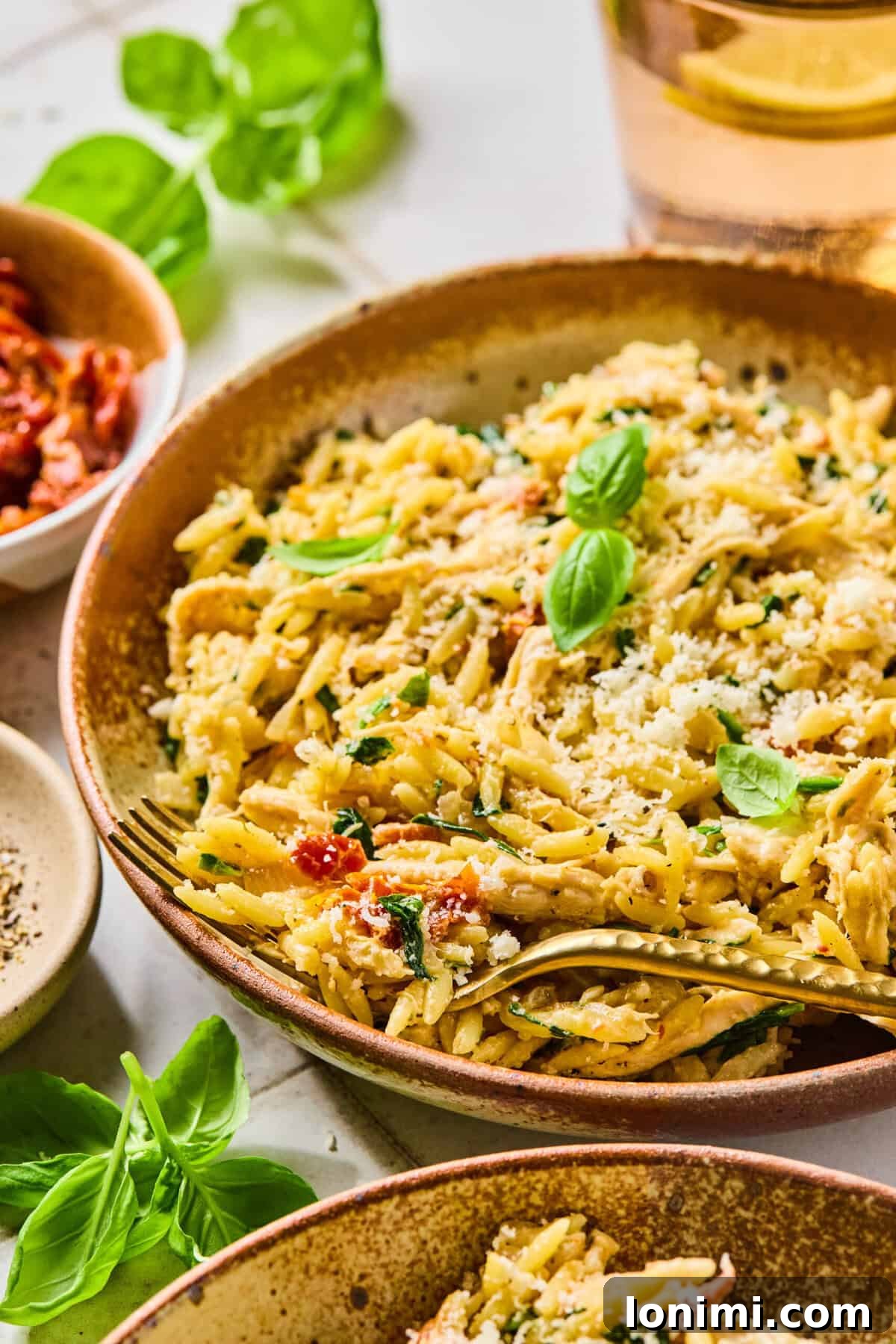 Irresistible Gluten Free Marry Me Chicken Orzo 2 Marry Me Chicken Orzo served in a bowl, garnished with fresh basil leaves, with a fork resting in the dish.