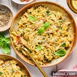 Marry Me Chicken Orzo in a bowl with a fork surrounded by ingredients and a pink napkin
