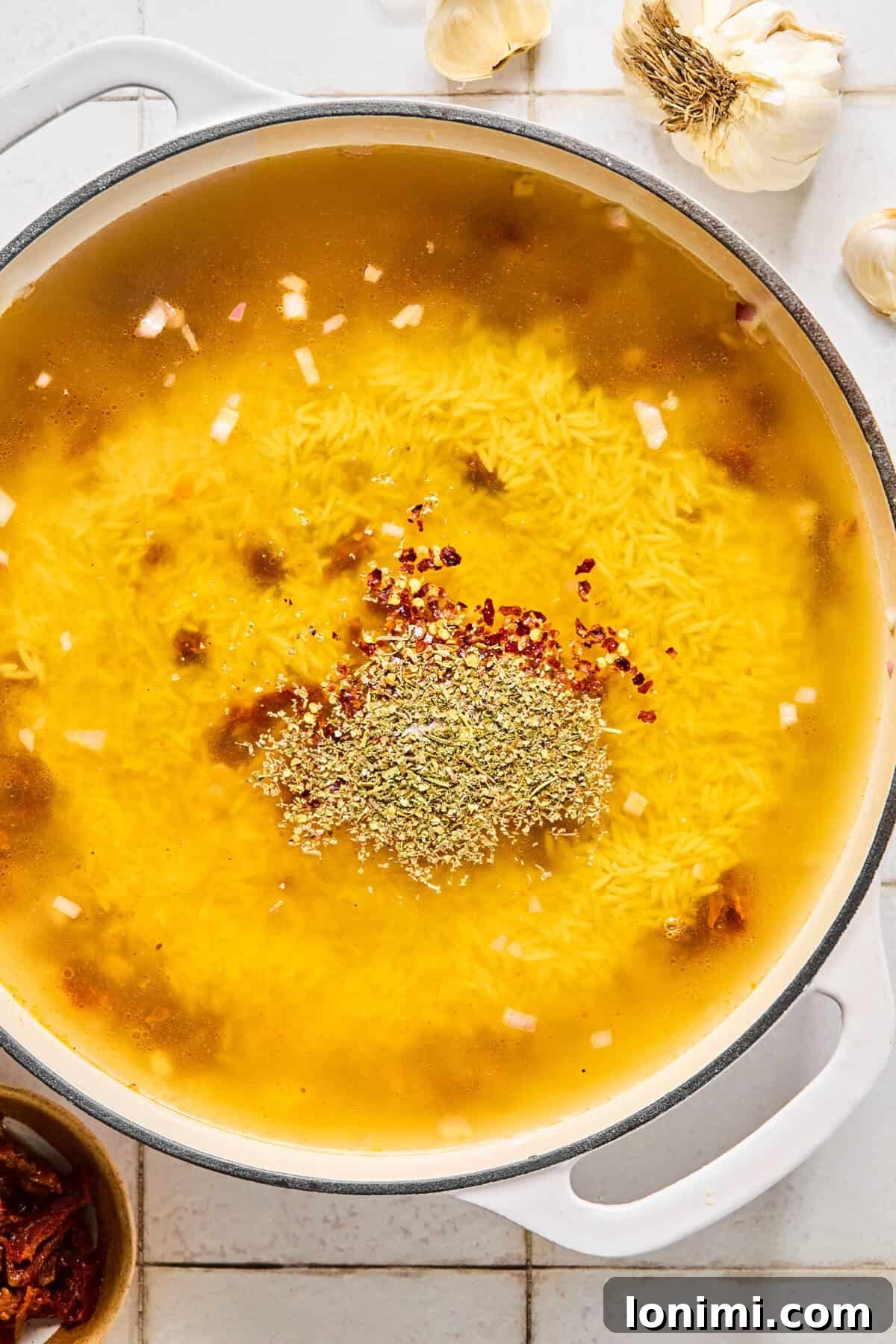 Irresistible Gluten Free Marry Me Chicken Orzo 5 Gluten-free orzo simmering in chicken broth with Italian seasoning and red pepper in a skillet.