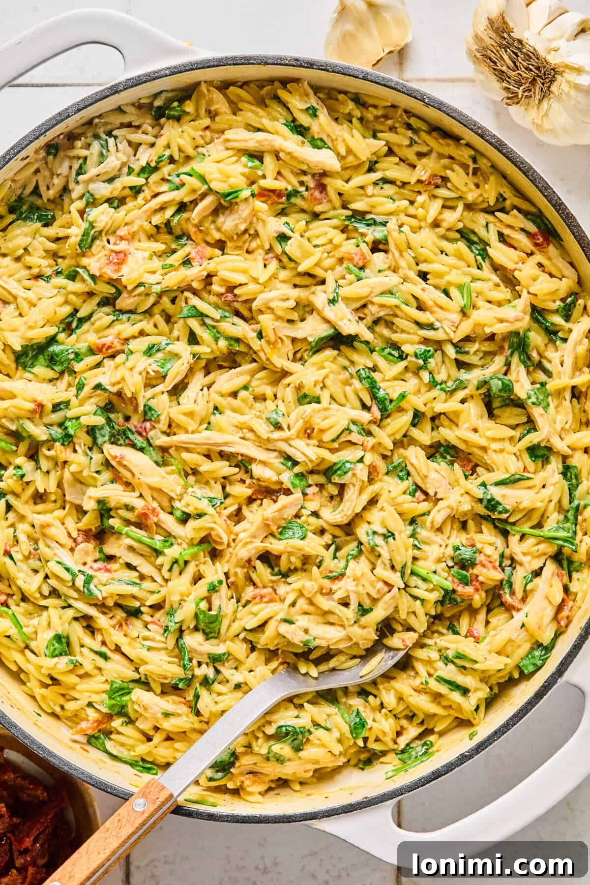 Irresistible Gluten Free Marry Me Chicken Orzo 7 Marry Me Chicken Orzo garnished with fresh basil and grated parmesan with a serving spoon resting in it.