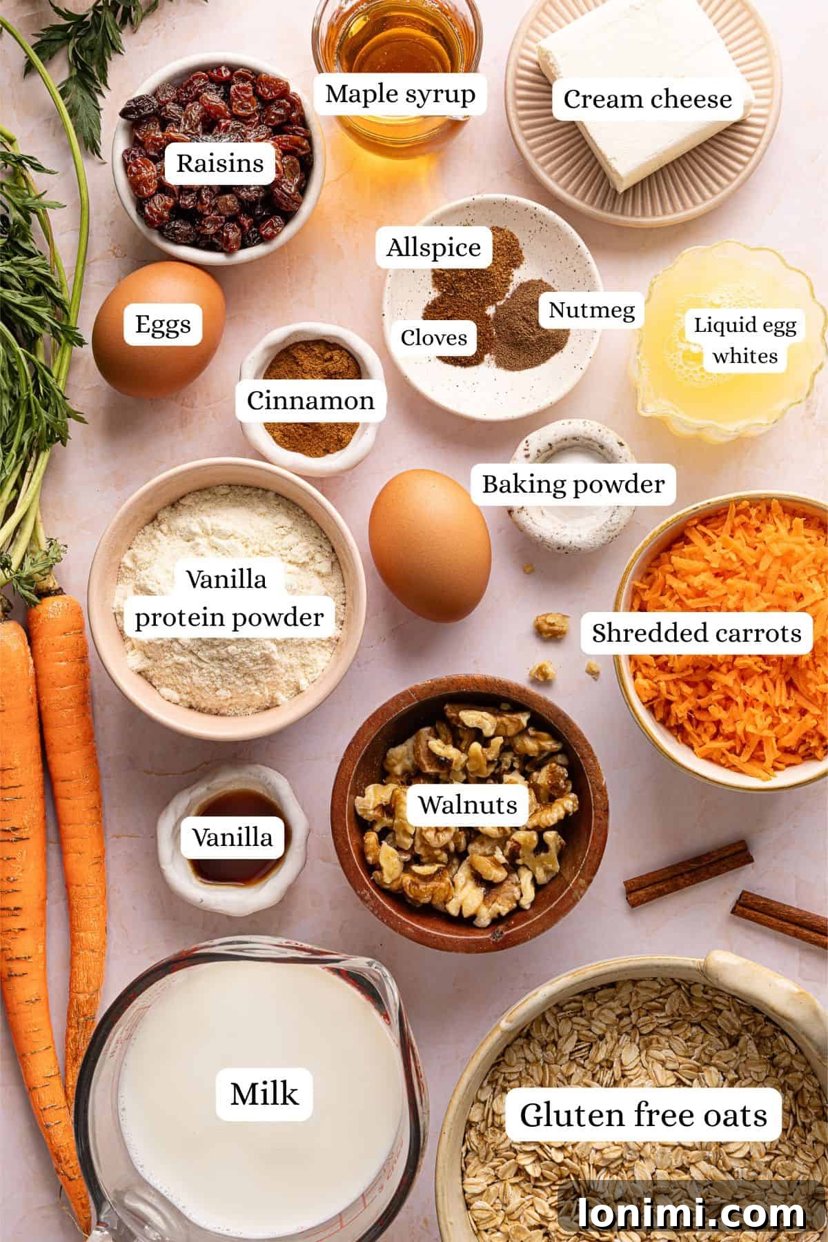 Ingredients for carrot cake baked oats labeled and laid out in nesting bowls on a light pink countertop.