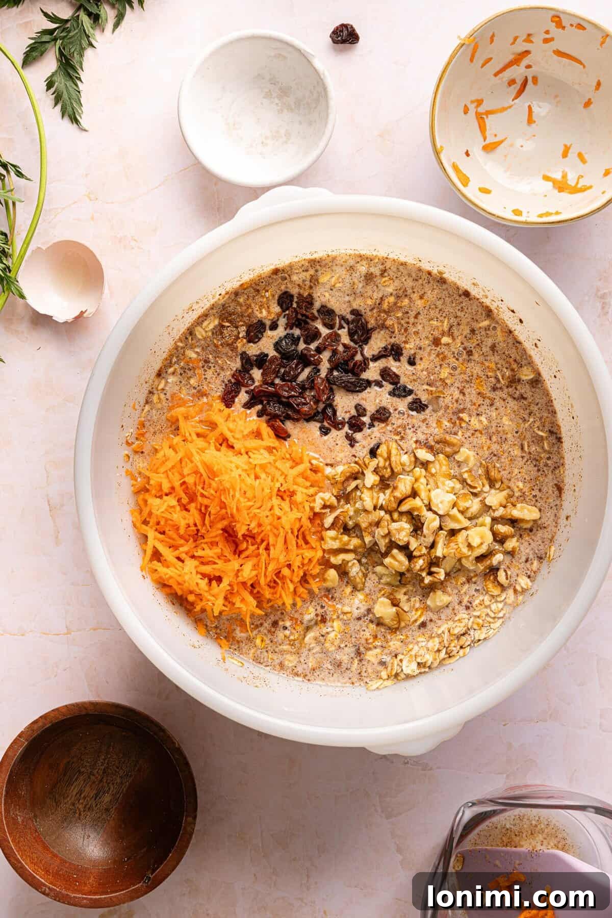Finely shredded carrots, raisins, and chopped walnuts folded into carrot cake baked oats batter.