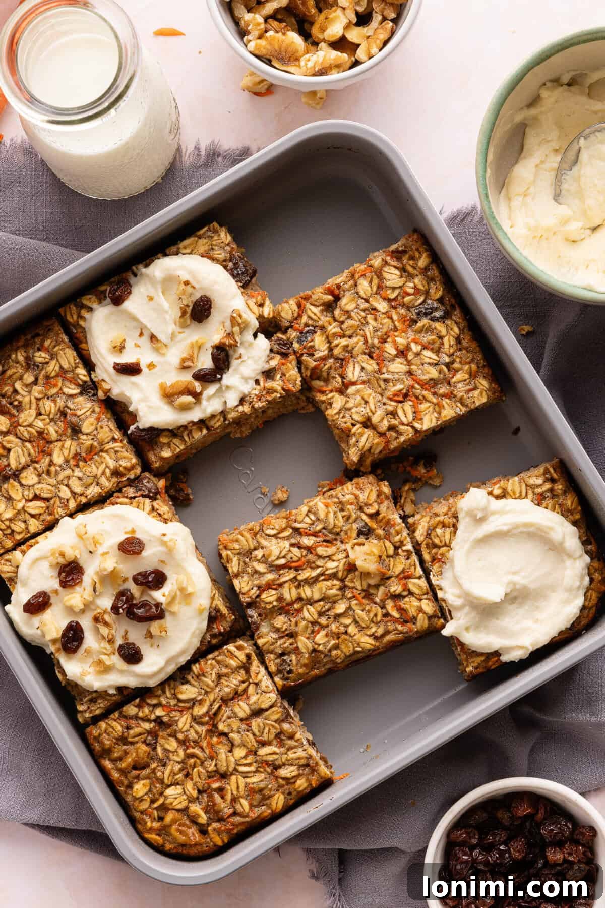 Sliced carrot cake baked oats; 3 of the slices have protein cream cheese frosting on them and are topped with raisins and walnuts.
