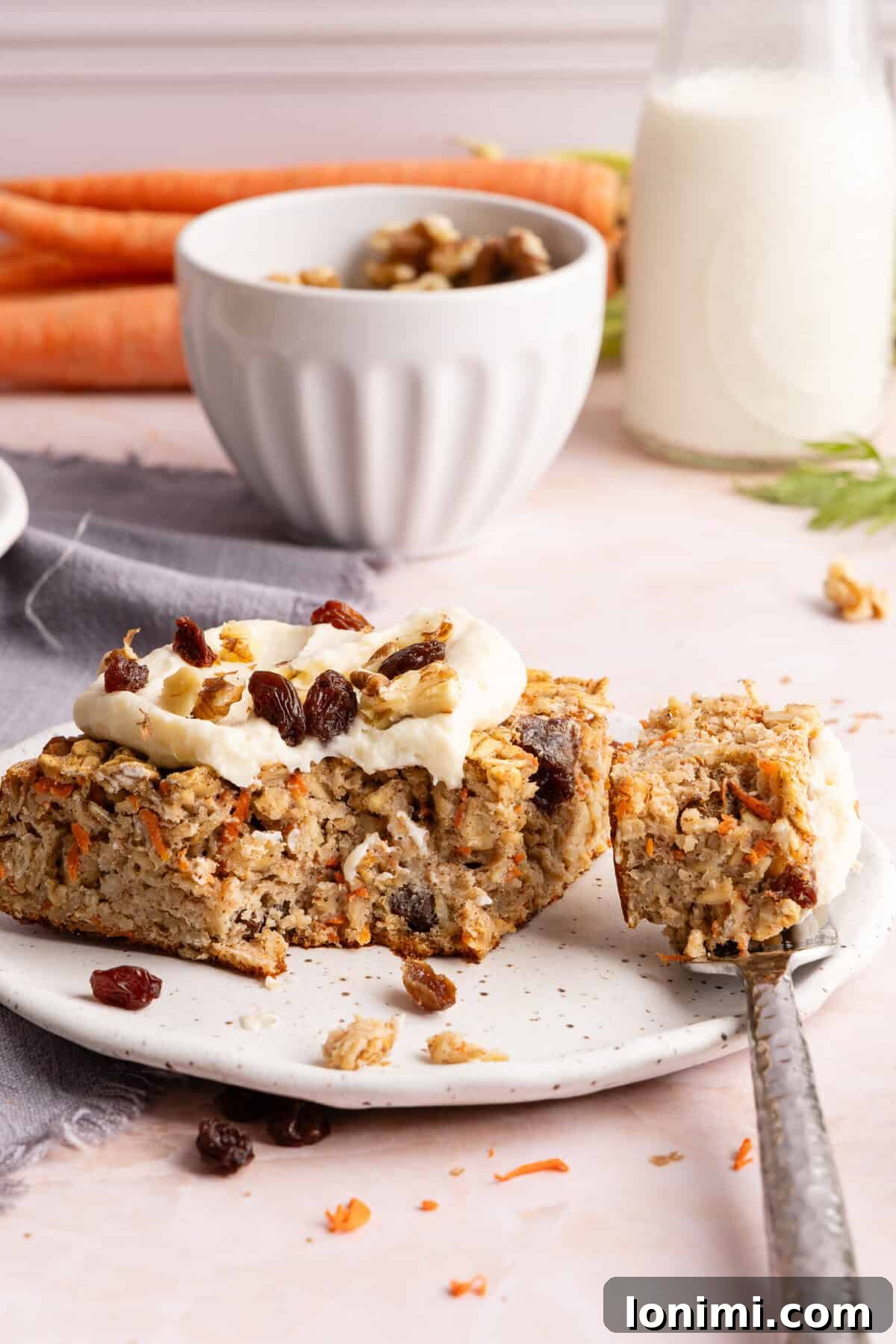 Close-up of carrot cake baked oats slice topped with protein cream cheese frosting, walnuts, and raisins. 